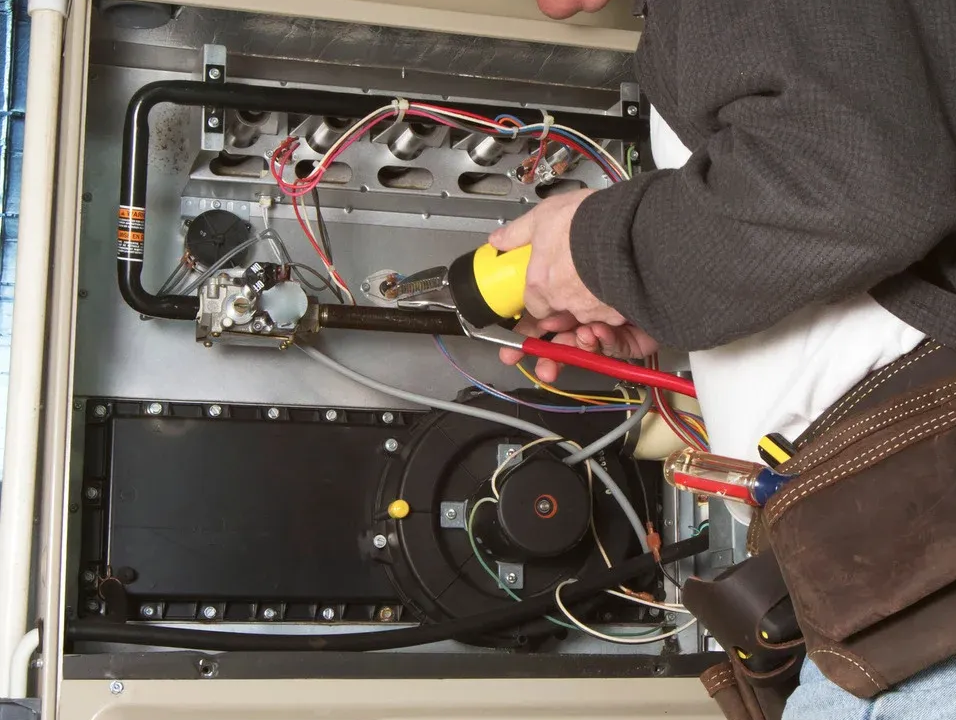 Person repairs furnace, using tools on internal components.