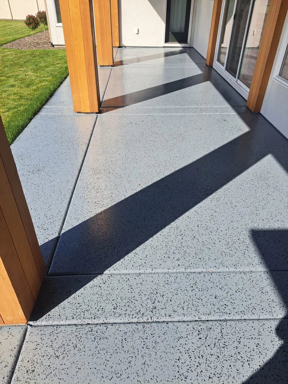 Gray concrete patio with wooden posts, shadow, and grass.
