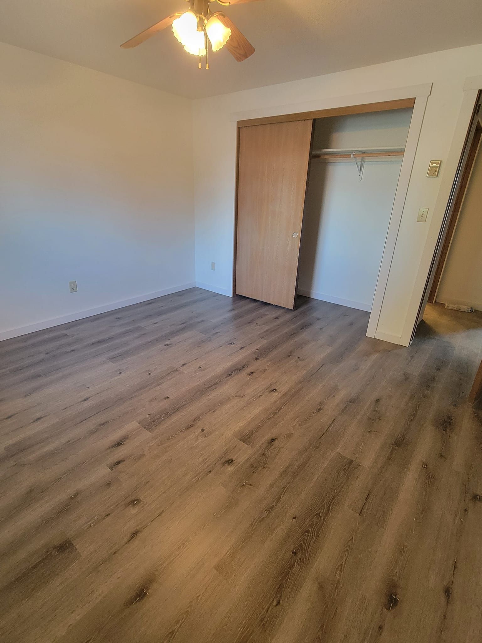 Empty bedroom with wood-look flooring, ceiling fan, and open closet doors.