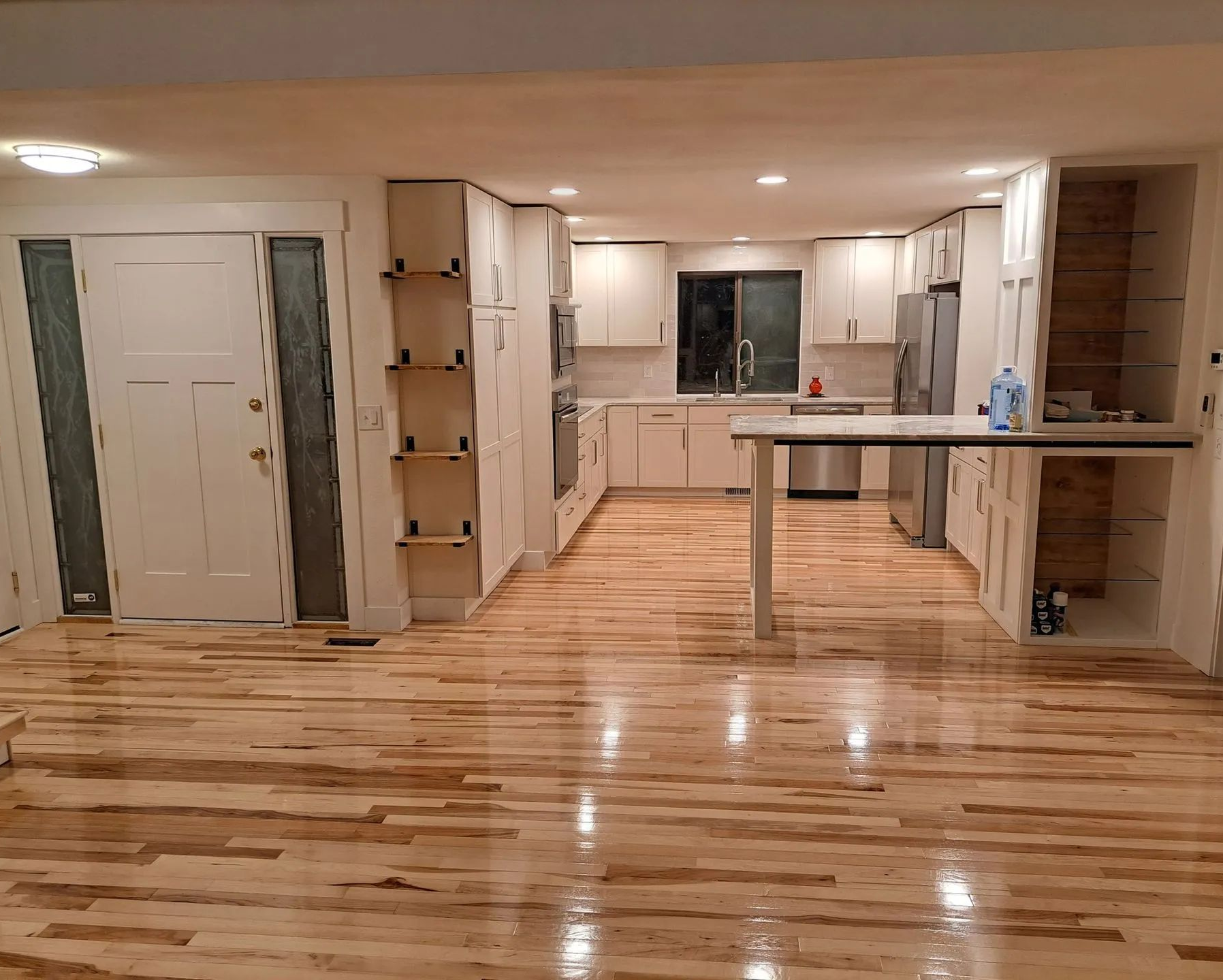 Empty modern kitchen and living room with glossy hardwood floors and recessed ceiling lights