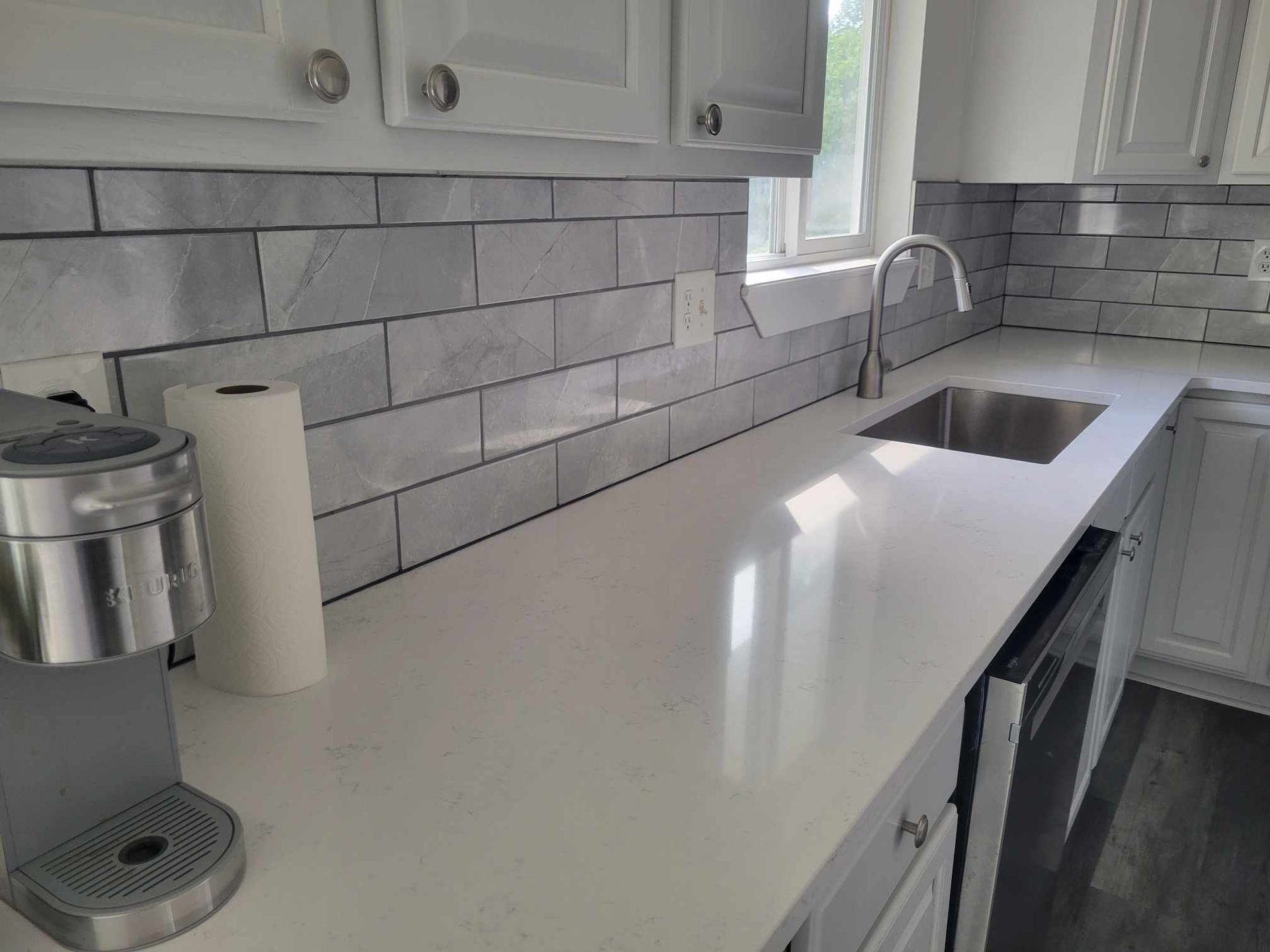 White kitchen with marble tile backsplash and shiny white countertop.