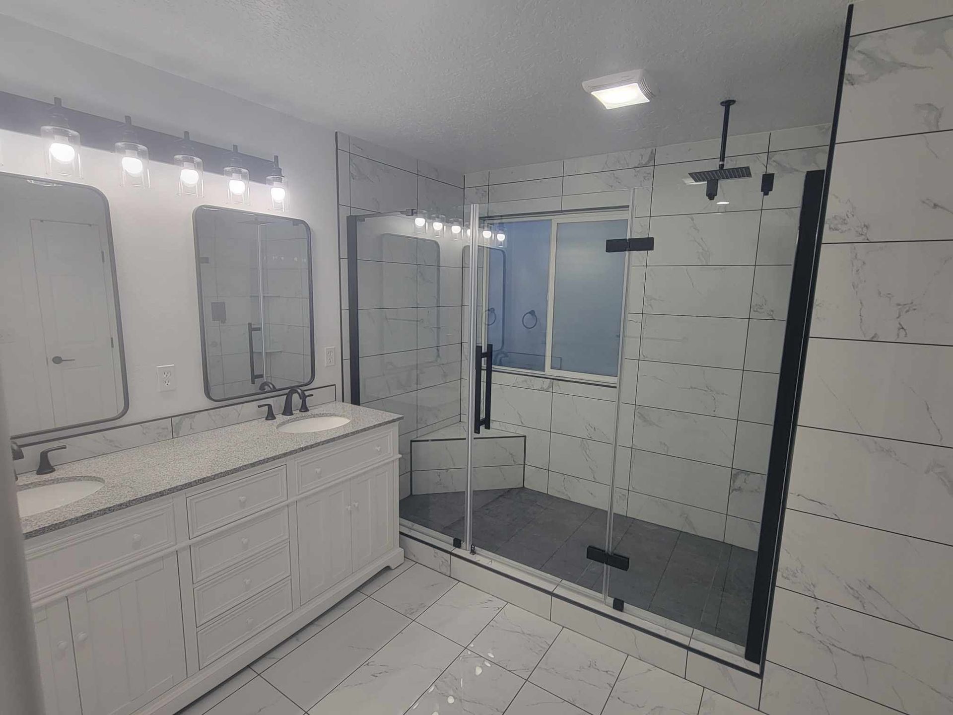 Modern white bathroom with marble tiles, glass shower, and black fixtures.