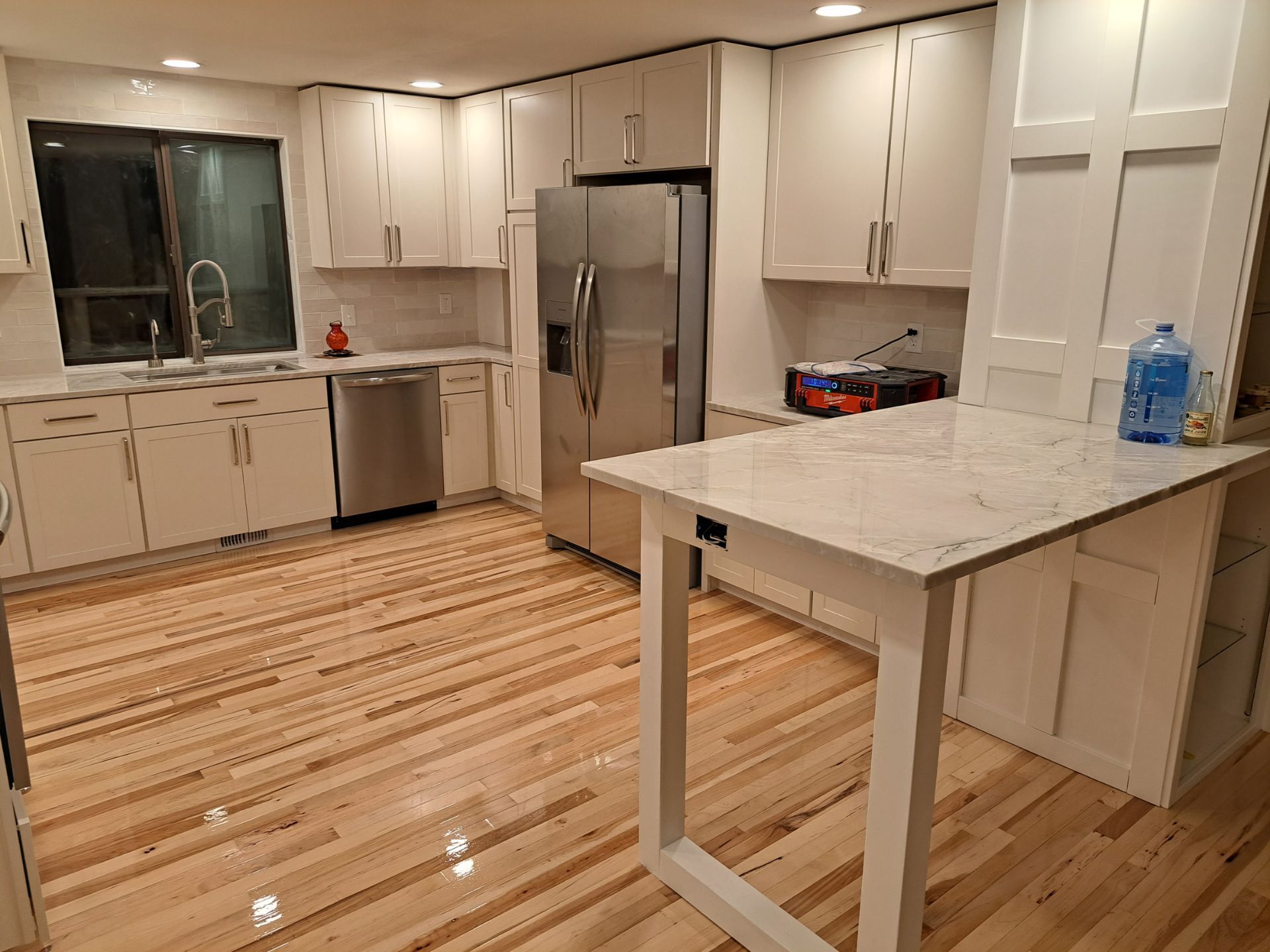 Bright white kitchen with stainless steel appliances, light wood floors, and a countertop table.
