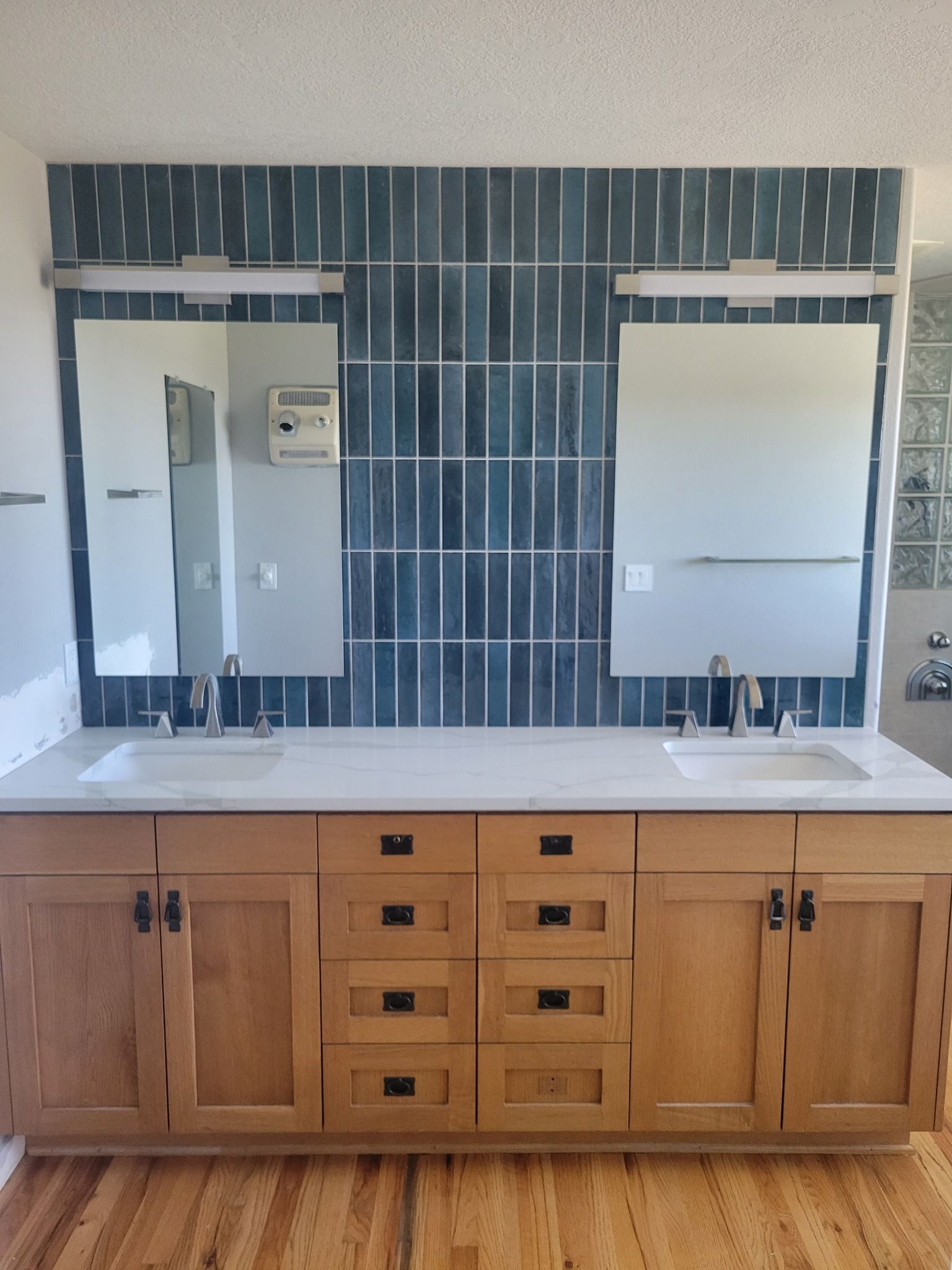 Bathroom with emerald green herringbone tile, white tub, unfinished wood vanity, mirror, and black fixtures.