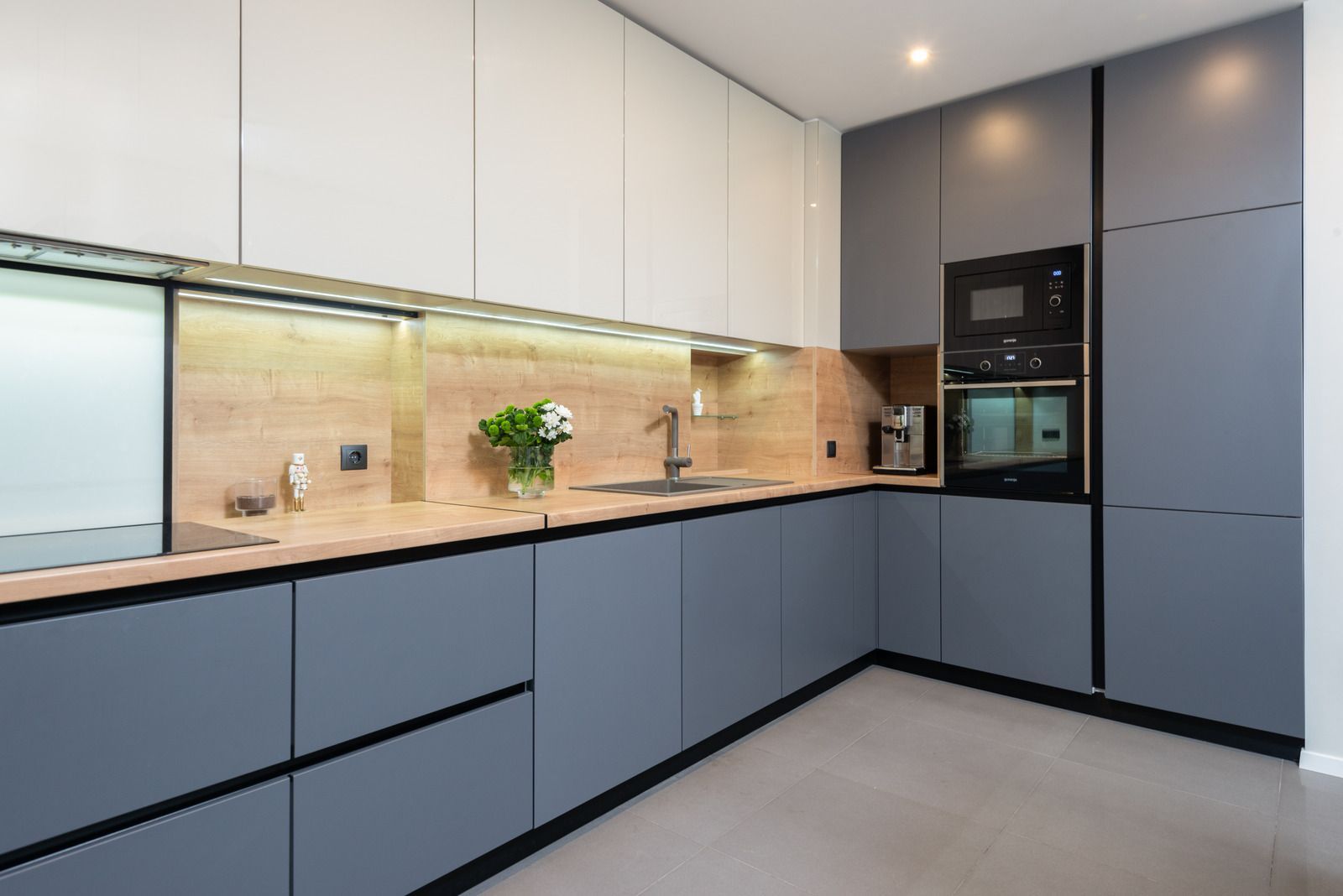 Modern kitchen with gray and white cabinets, wood countertop, built-in appliances, and recessed lighting.