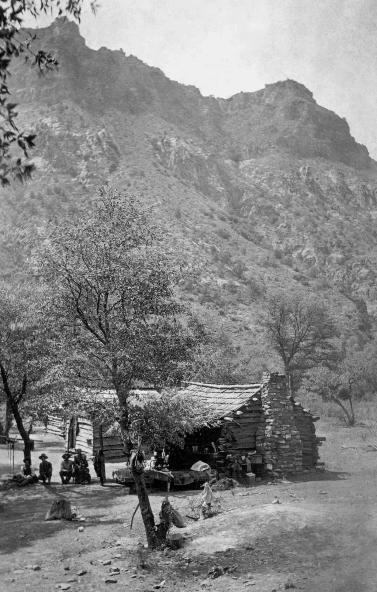 Mountain village with a thatched hut, trees, and people standing along a dirt path