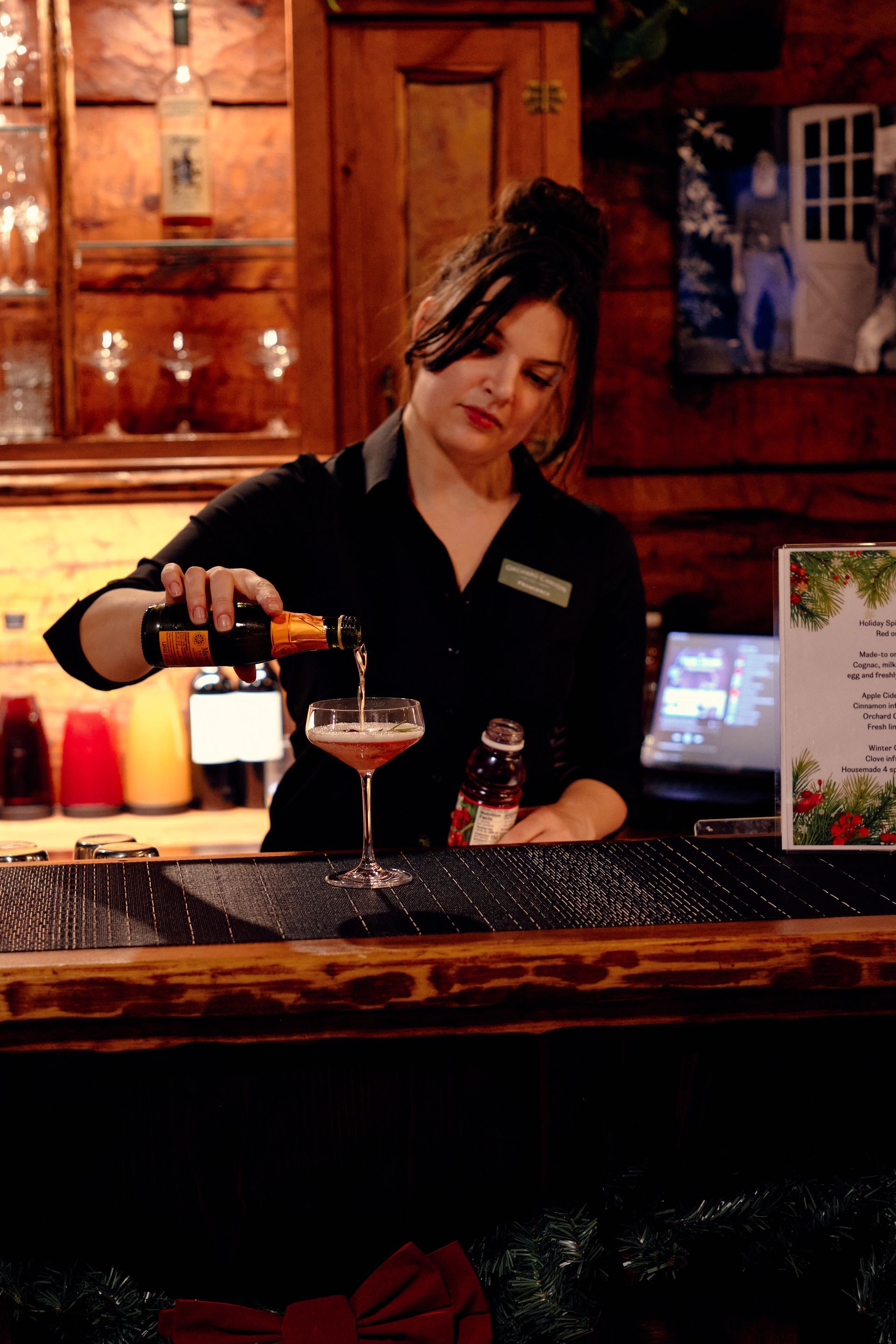 Bartender pouring a cocktail at a wooden bar with bottles and warm amber lighting