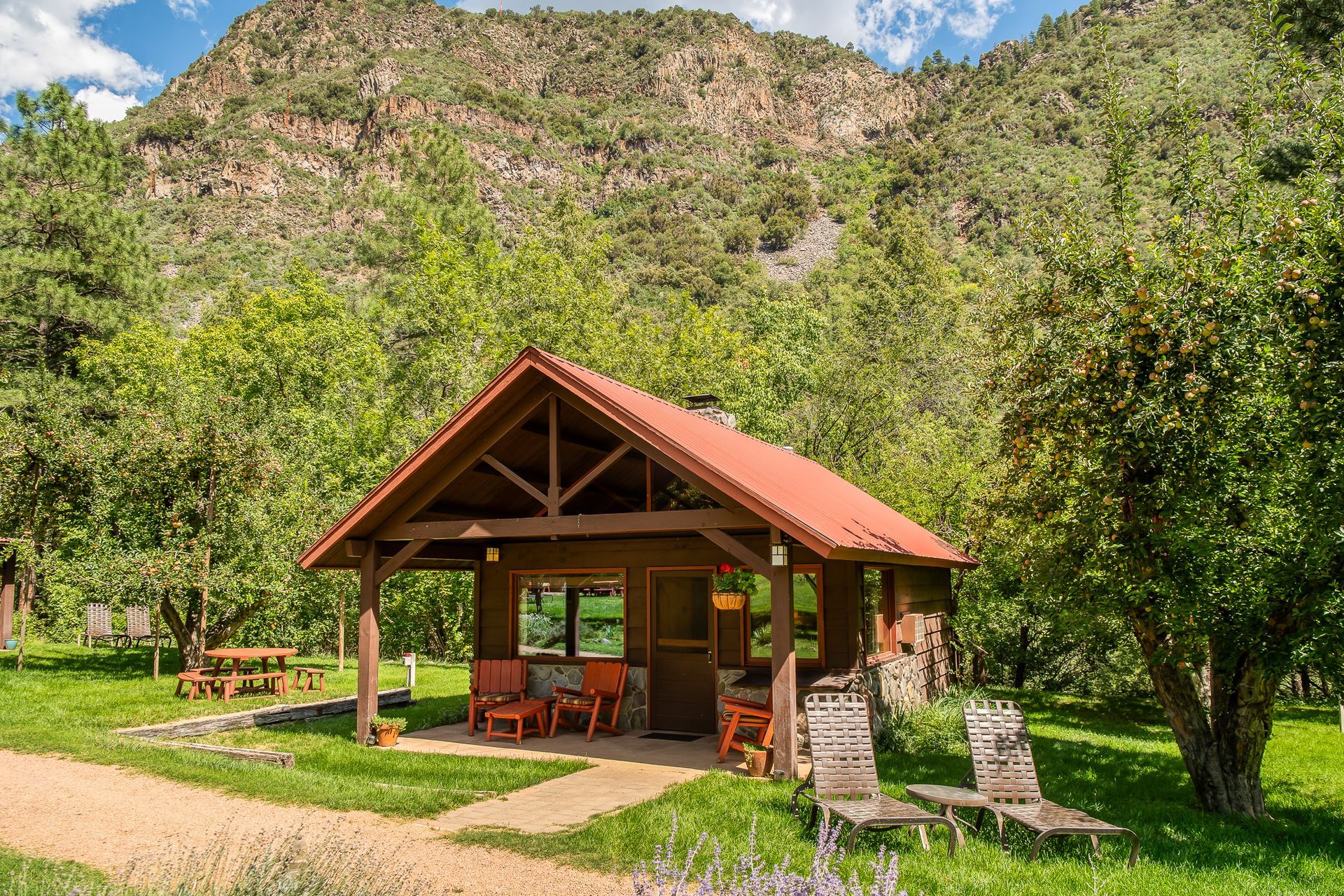 Small wooden cabin with red roof in a lush green valley, with mountains in the background
