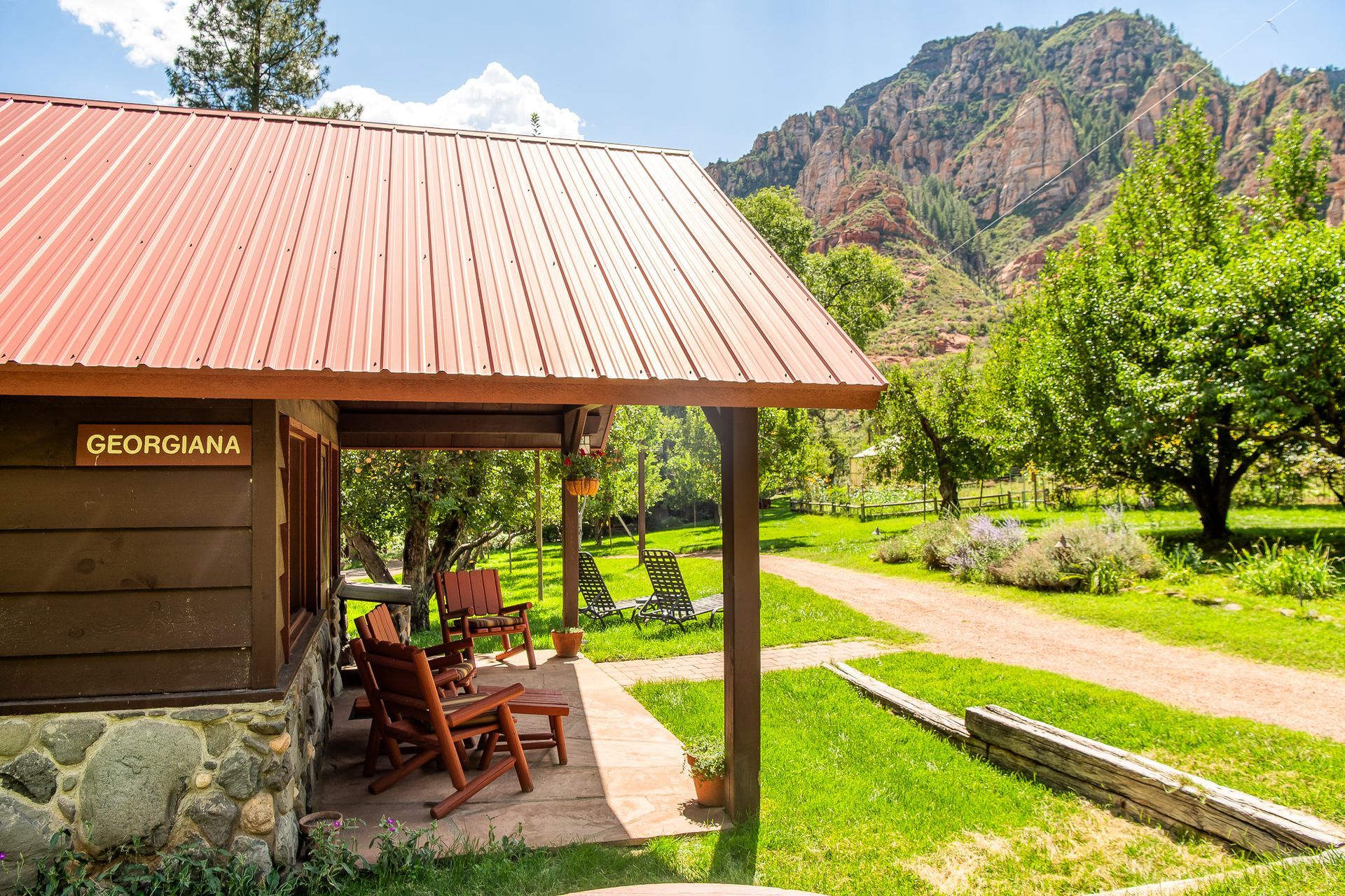 Rustic porch beside a sunny garden path with mountains and trees in the background