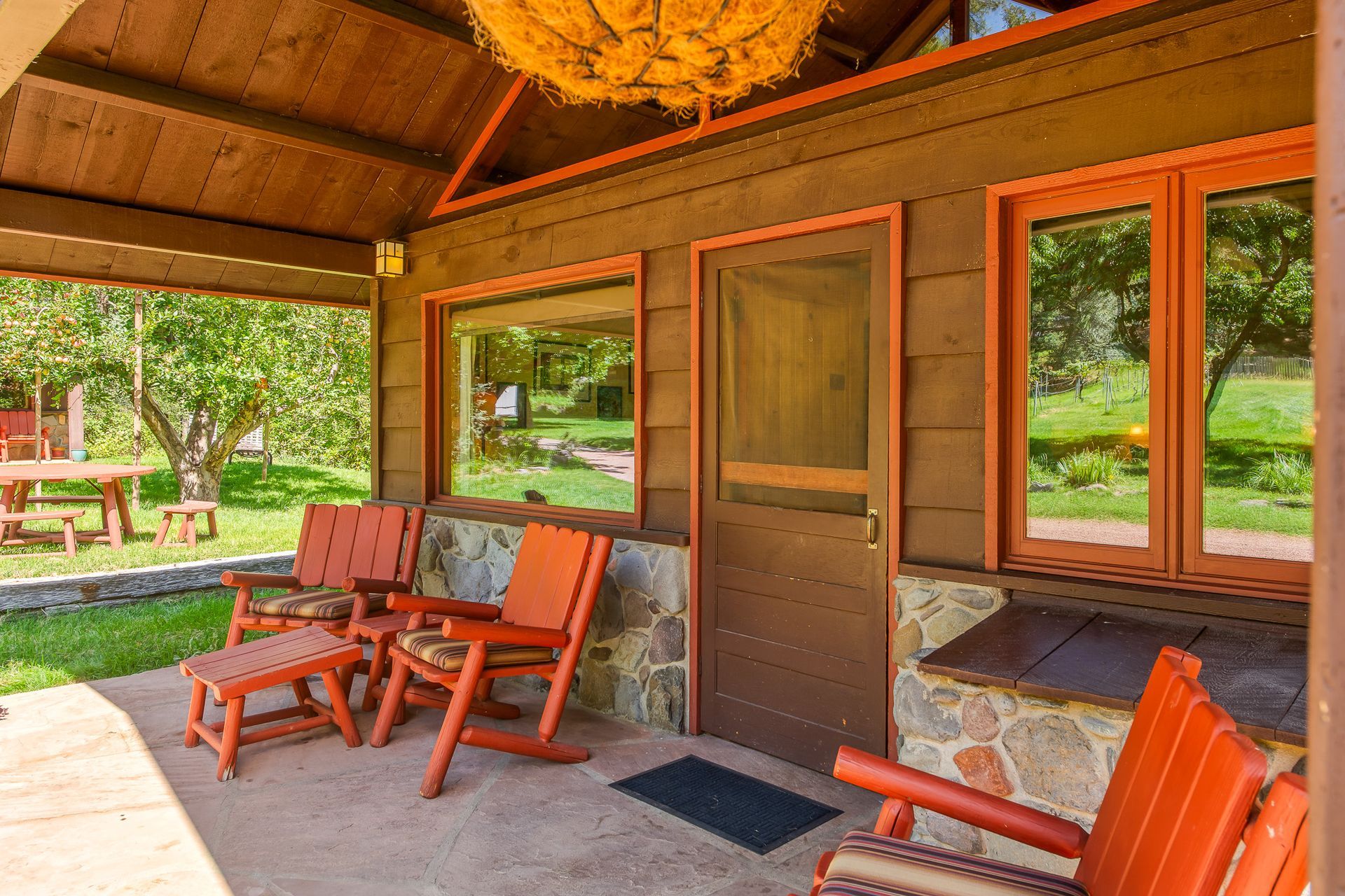 Covered porch with orange chairs, wooden door, and large windows overlooking a green yard