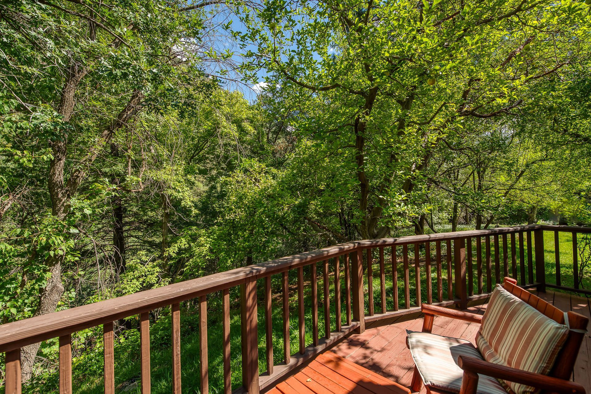 Wooden deck with striped chair overlooking a lush green wooded landscape
