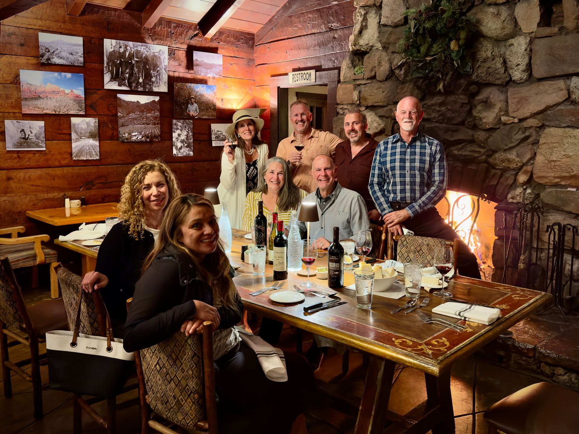 Group of people dining and posing in a cozy brick-walled restaurant with a long wooden table and warm lighting