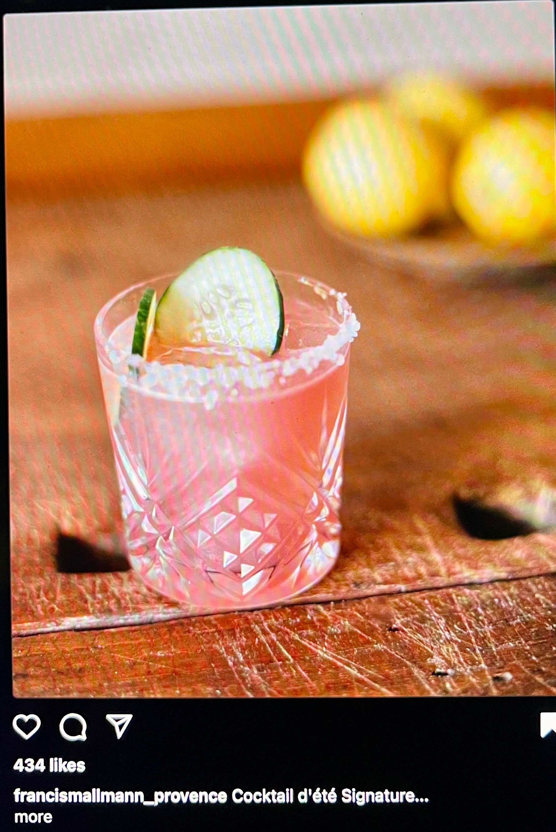 Pink cocktail in a crystal glass with a lemon garnish on a wooden table, blurred lemons in the background