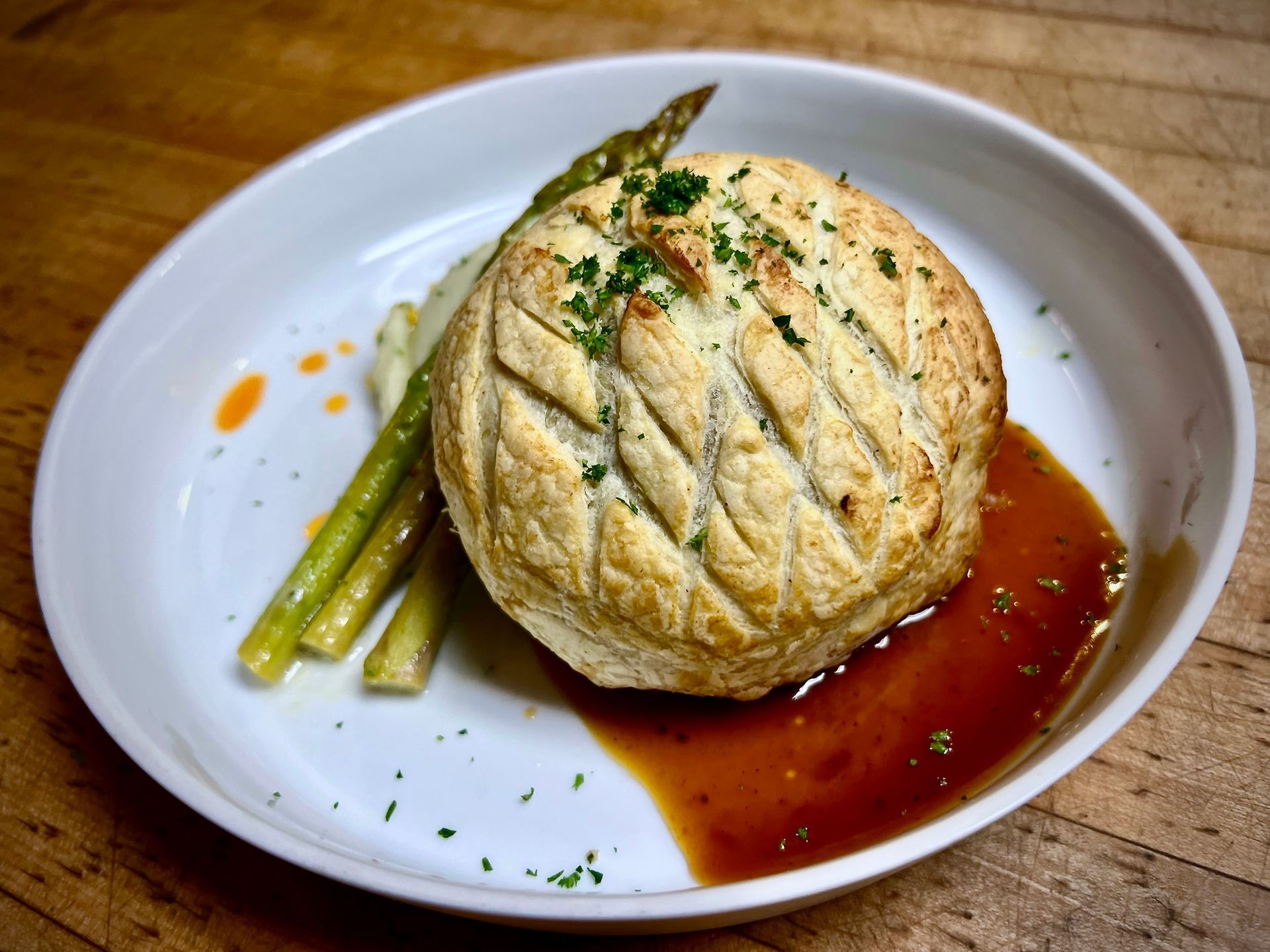 Baked pastry on a white plate with asparagus and brown sauce, sprinkled with herbs