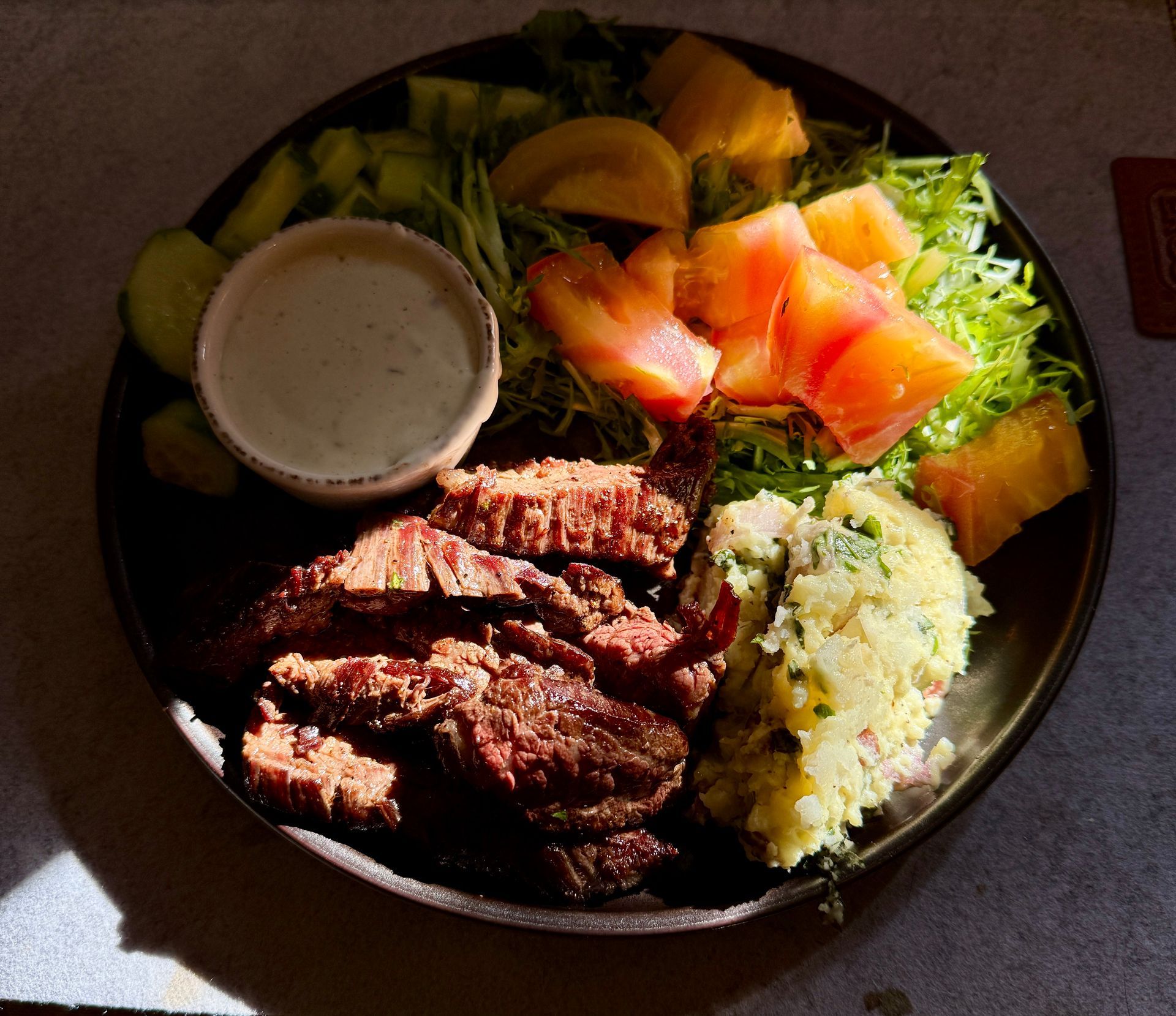 Plate of fried meat, rice, salad, and fruit with a small dipping sauce cup in sunlight