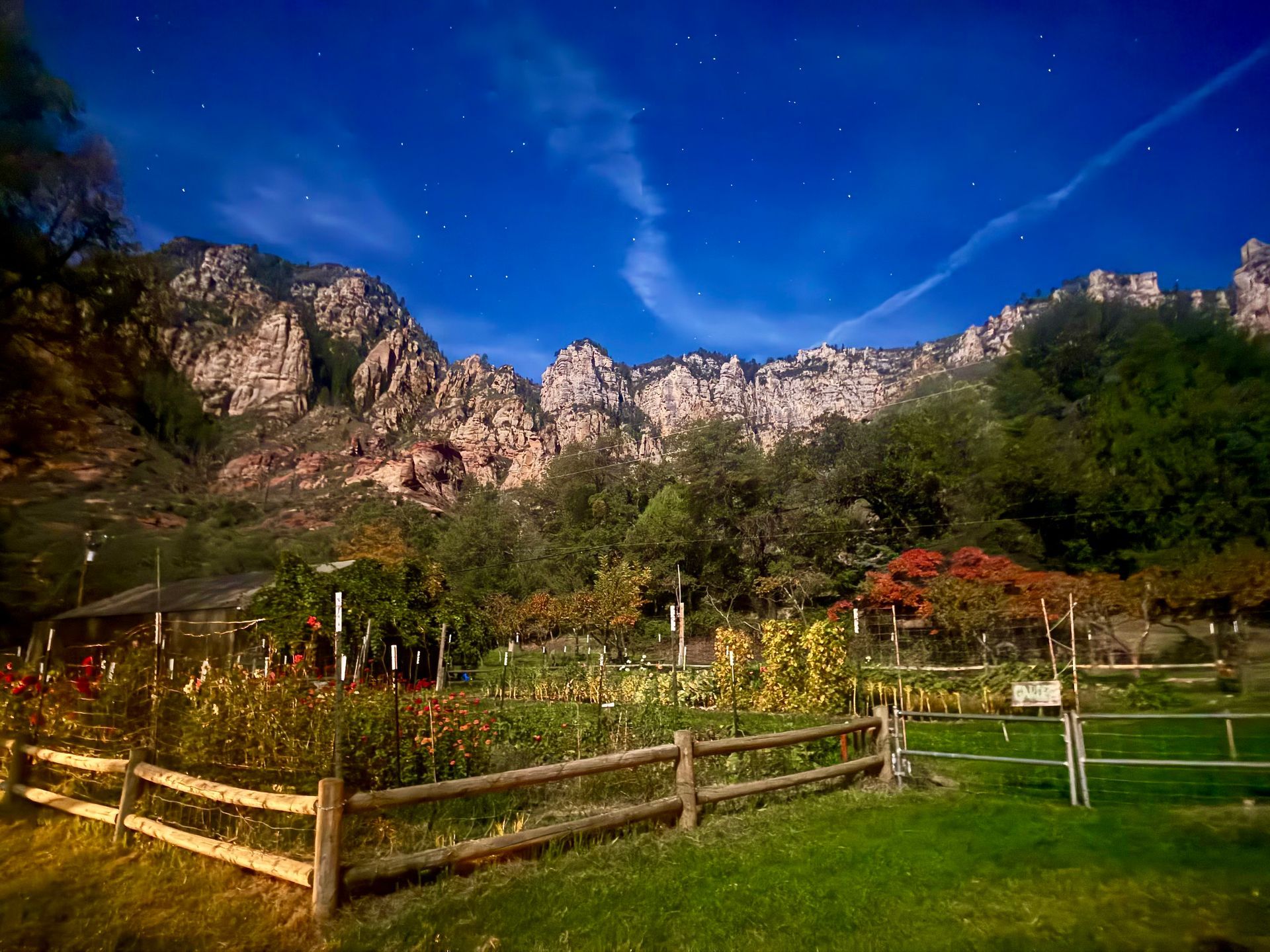 Wooden fence and wildflowers in a green meadow beneath rocky mountains and a bright blue sky
