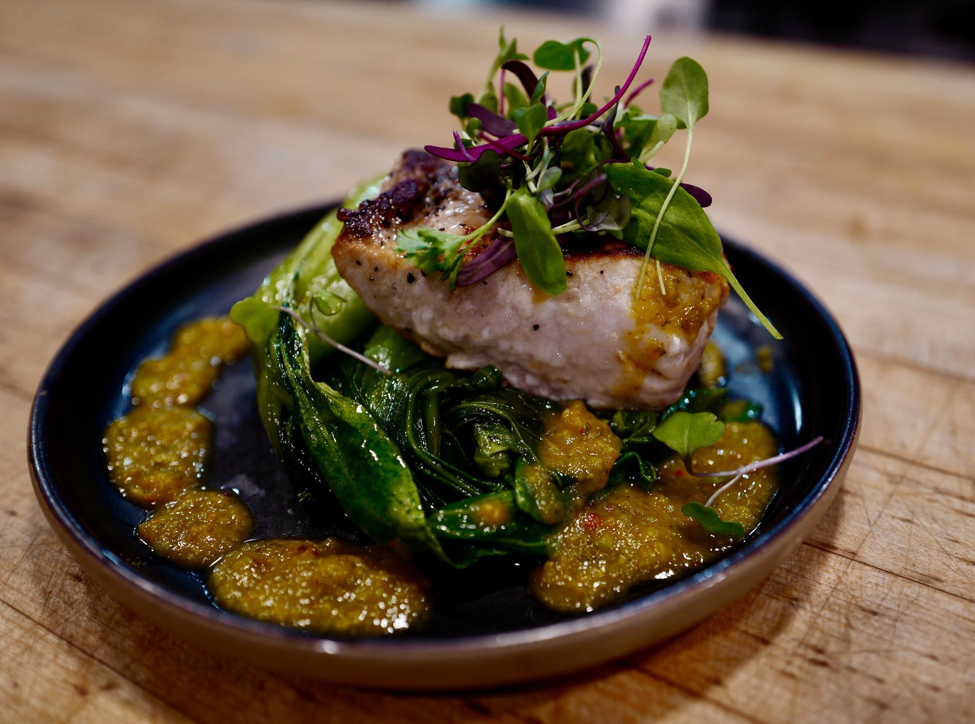 Seared fish atop greens with yellow sauce on a black plate