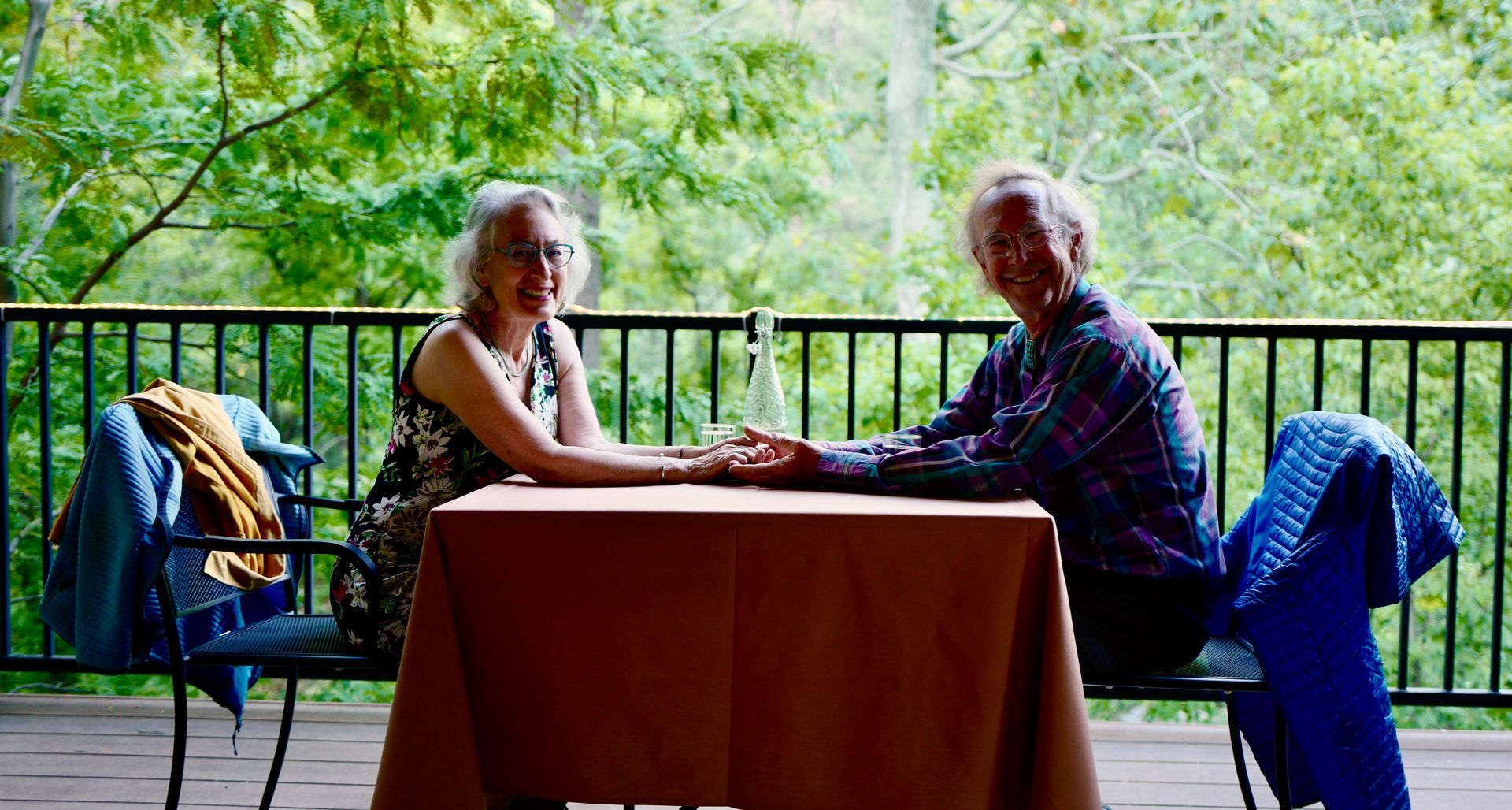 Two people sitting at a table on a balcony with greenery in the background