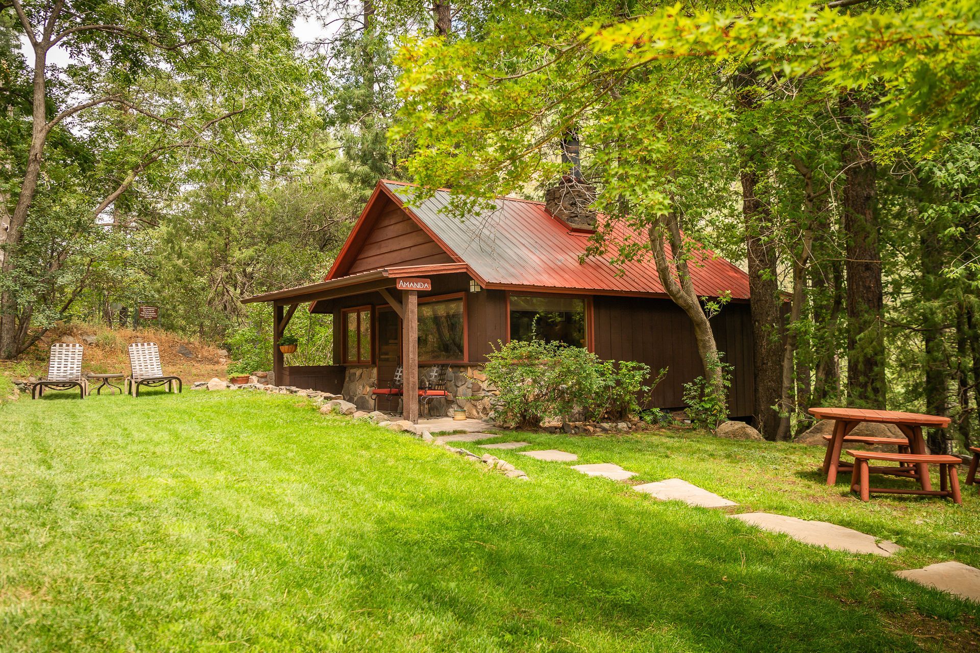 Wooden cabin in a lush green forest clearing with picnic tables and a stone path