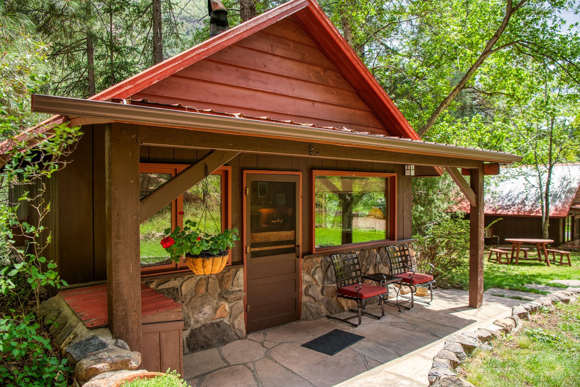 Small rustic cabin with a red roof, front porch, and wooden door in a leafy garden setting