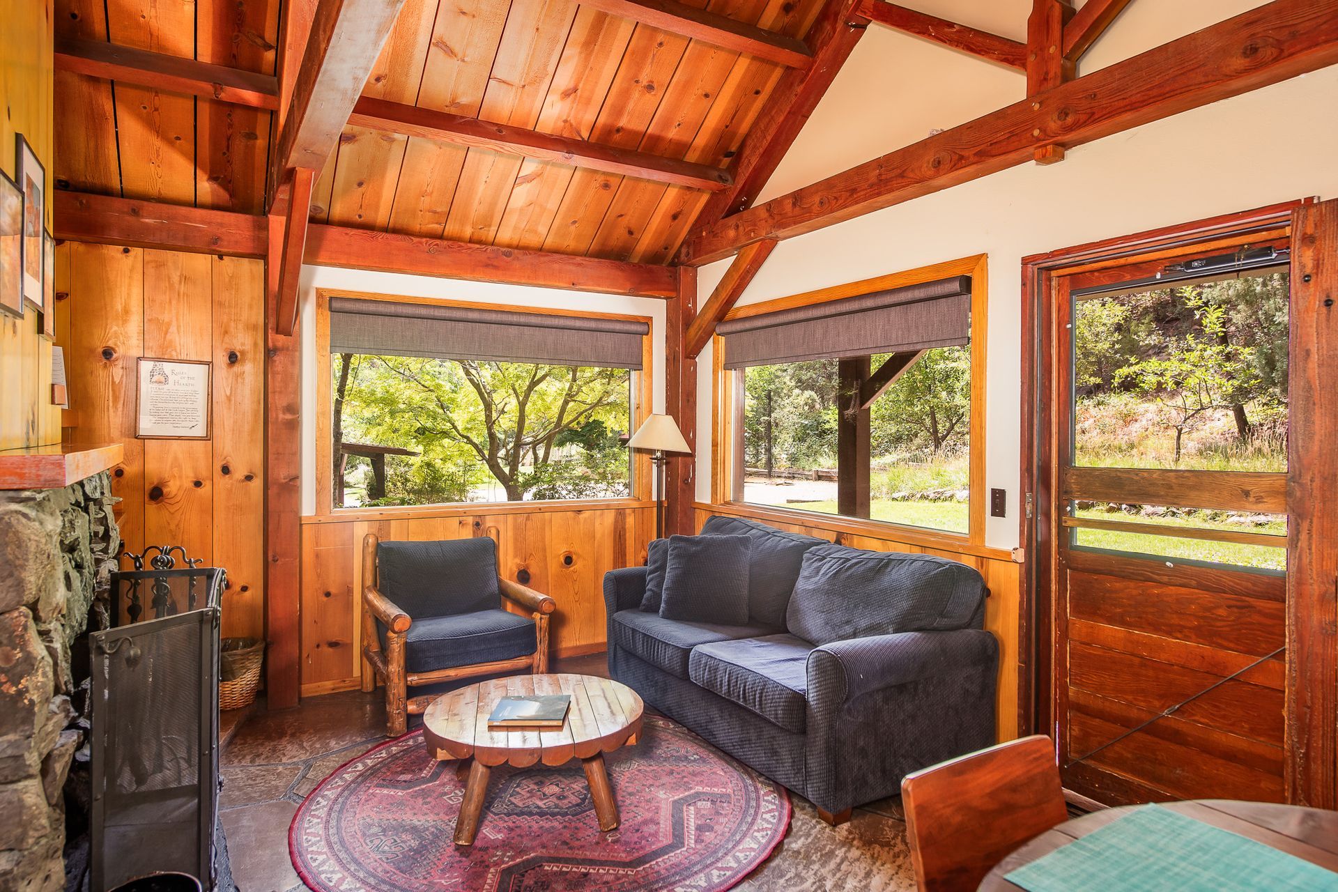 Rustic cabin living room with wood beams, a dark sofa, and large windows overlooking greenery