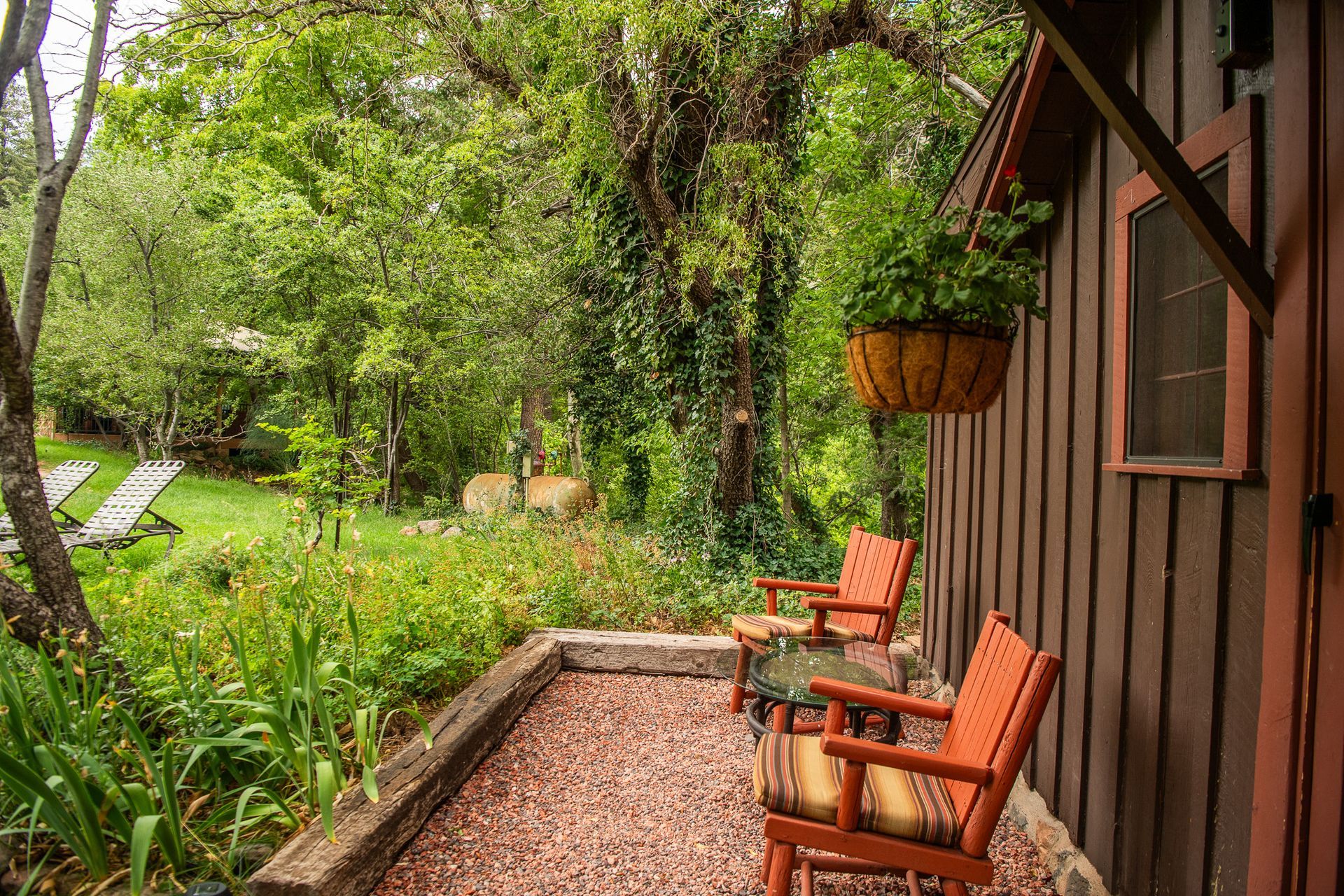 Covered patio with two orange chairs beside a lush green garden and gravel path