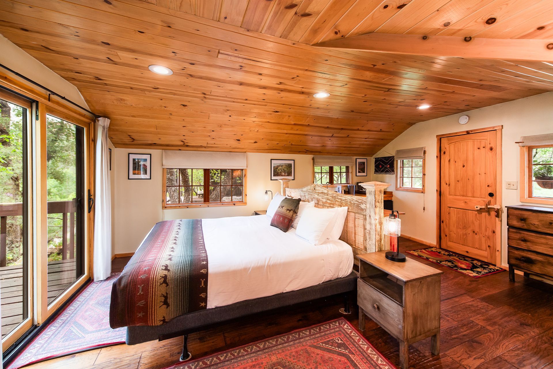 Cozy bedroom with wood-paneled ceiling, large bed, and sliding glass doors overlooking greenery