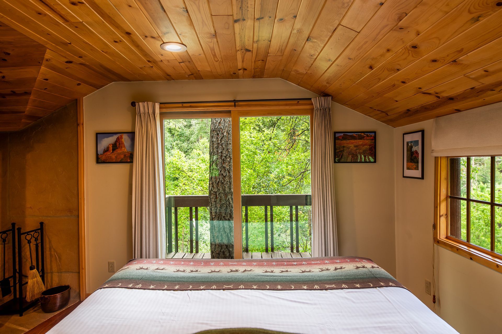 Wooden cabin bedroom with a bed, sloped ceiling, and large windows overlooking green trees