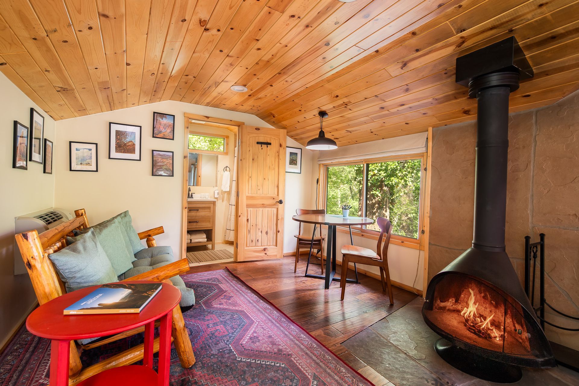Cozy wood-paneled living room with a black stove, colorful rug, and small table by a window.