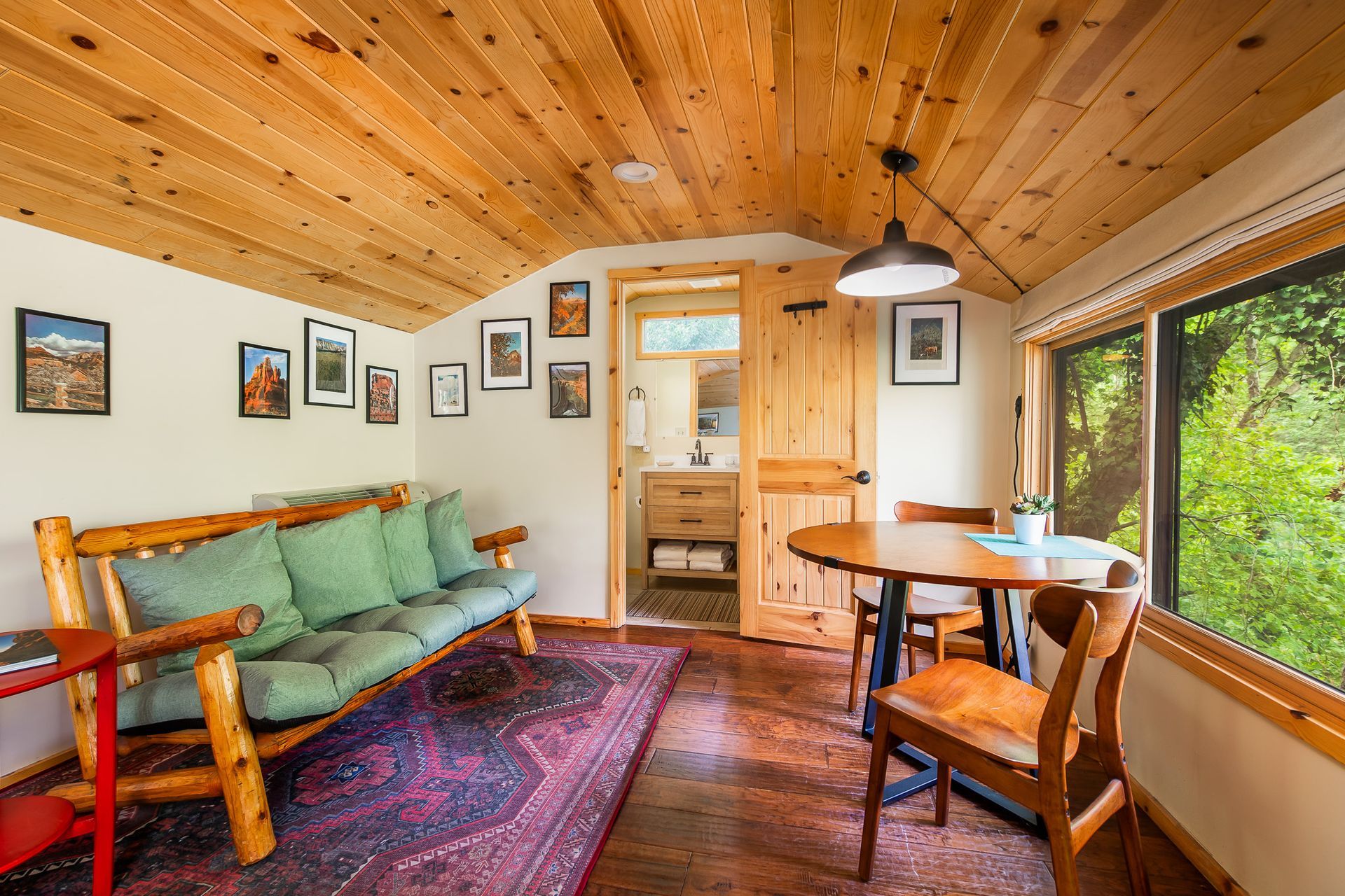 Cozy cabin living room with wood walls, green sofa, round table, and large window view