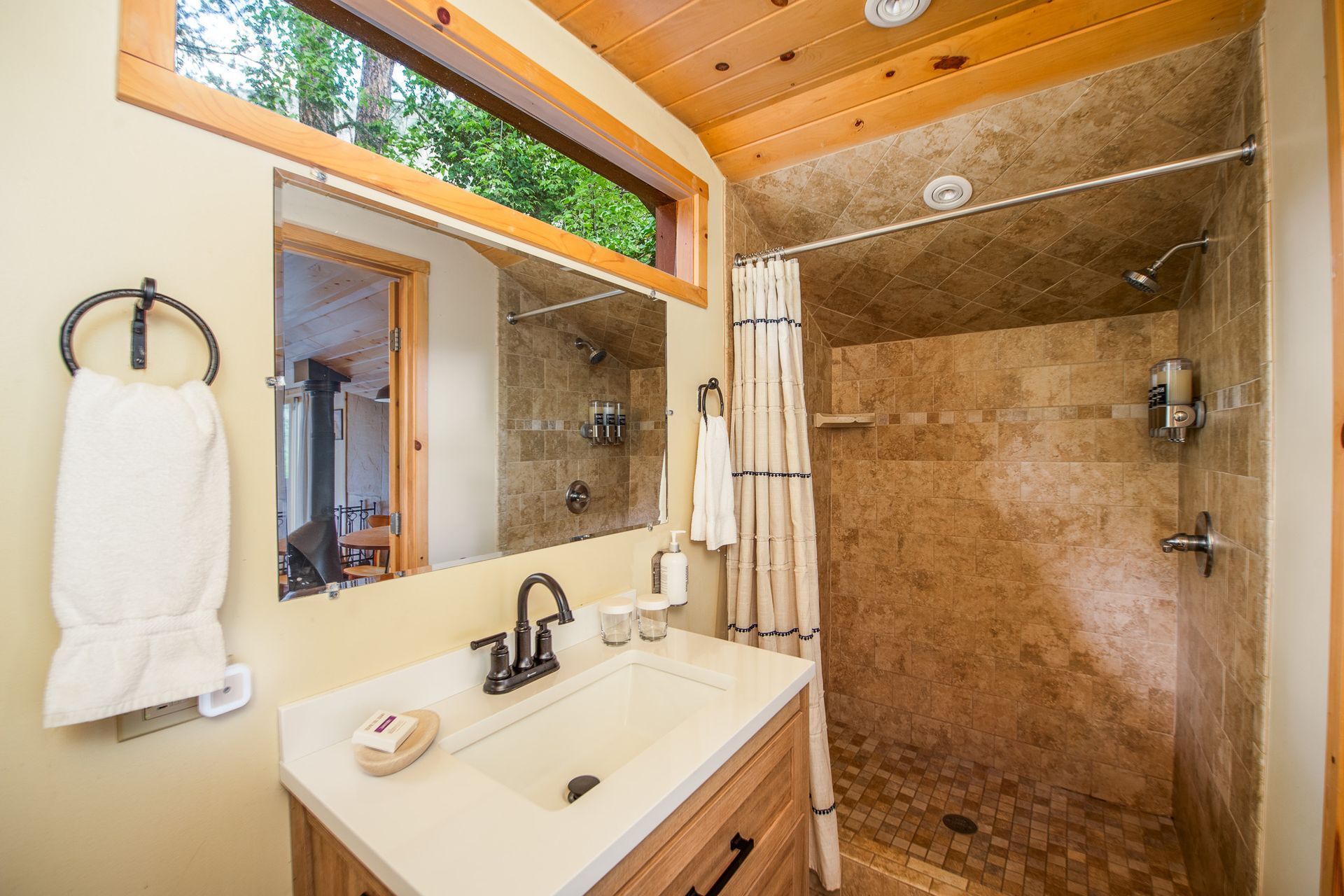 Bathroom with beige tile shower, white sink, wooden ceiling, and mirror above the vanity
