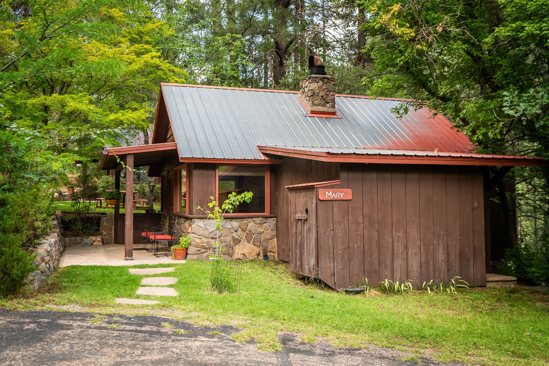 Rustic wooden cabin with a red metal roof, surrounded by trees and greenery