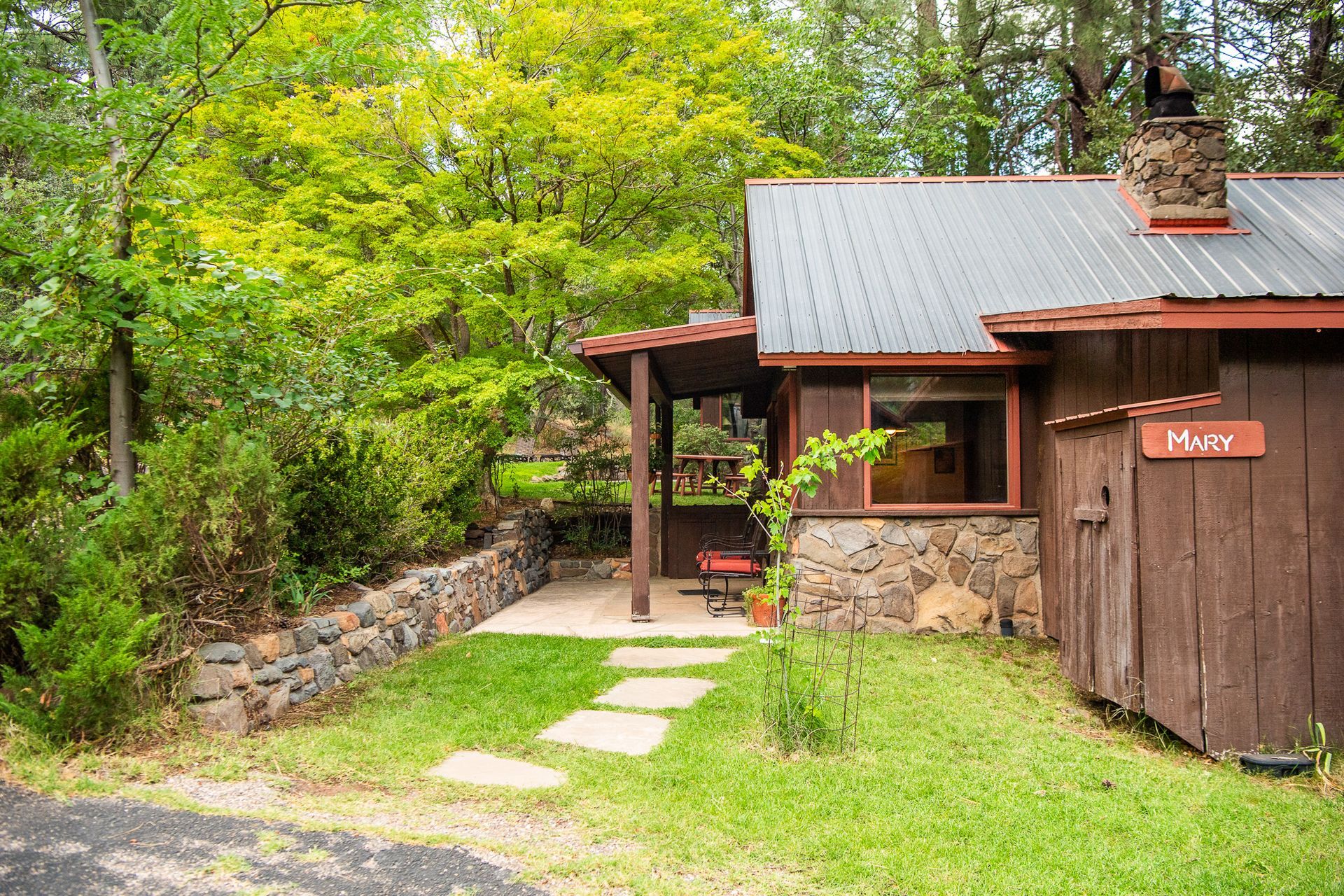 Rustic cabin with stone path, green yard, and trees surrounding it