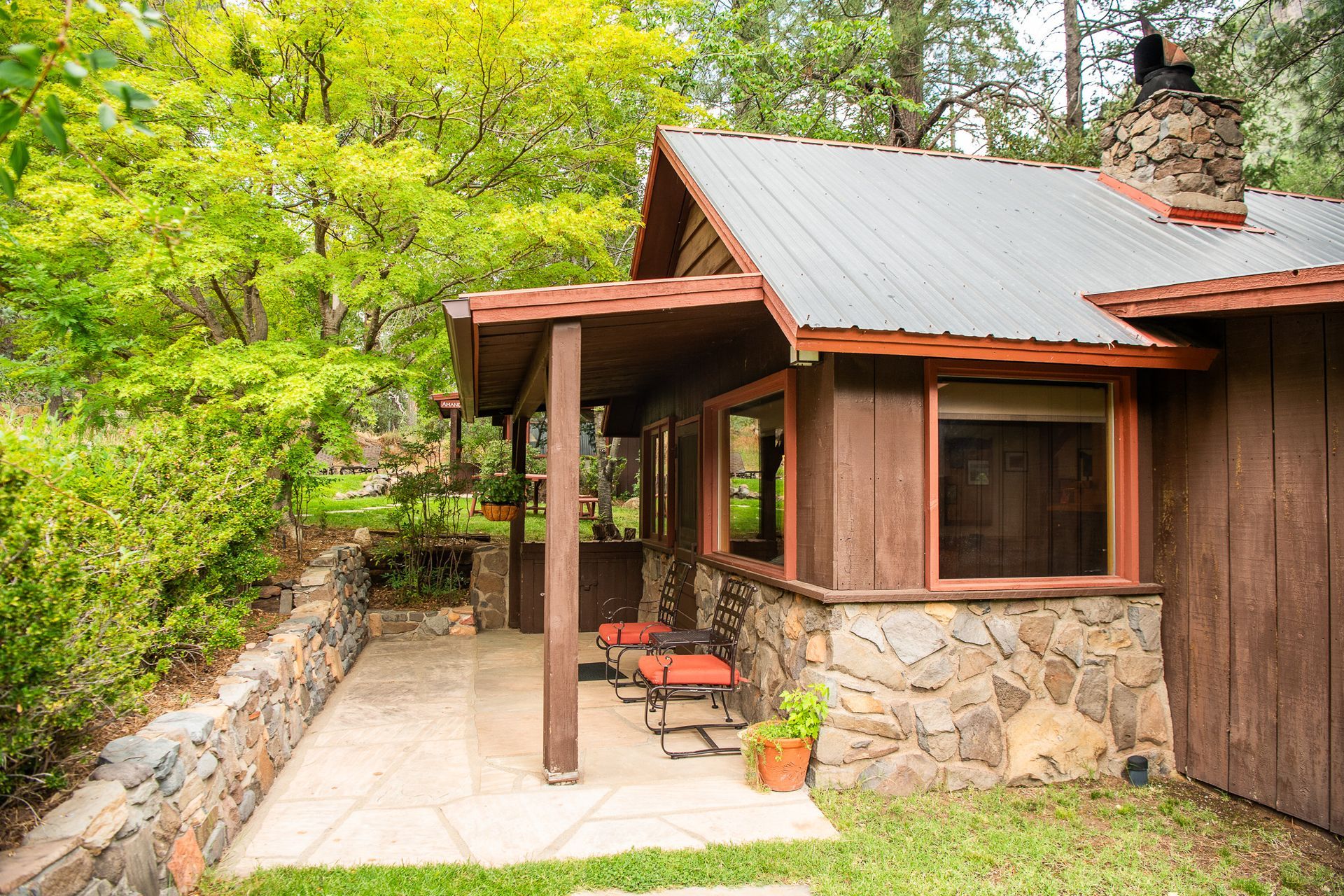 Rustic cabin porch with stone wall, red chairs, and lush green trees