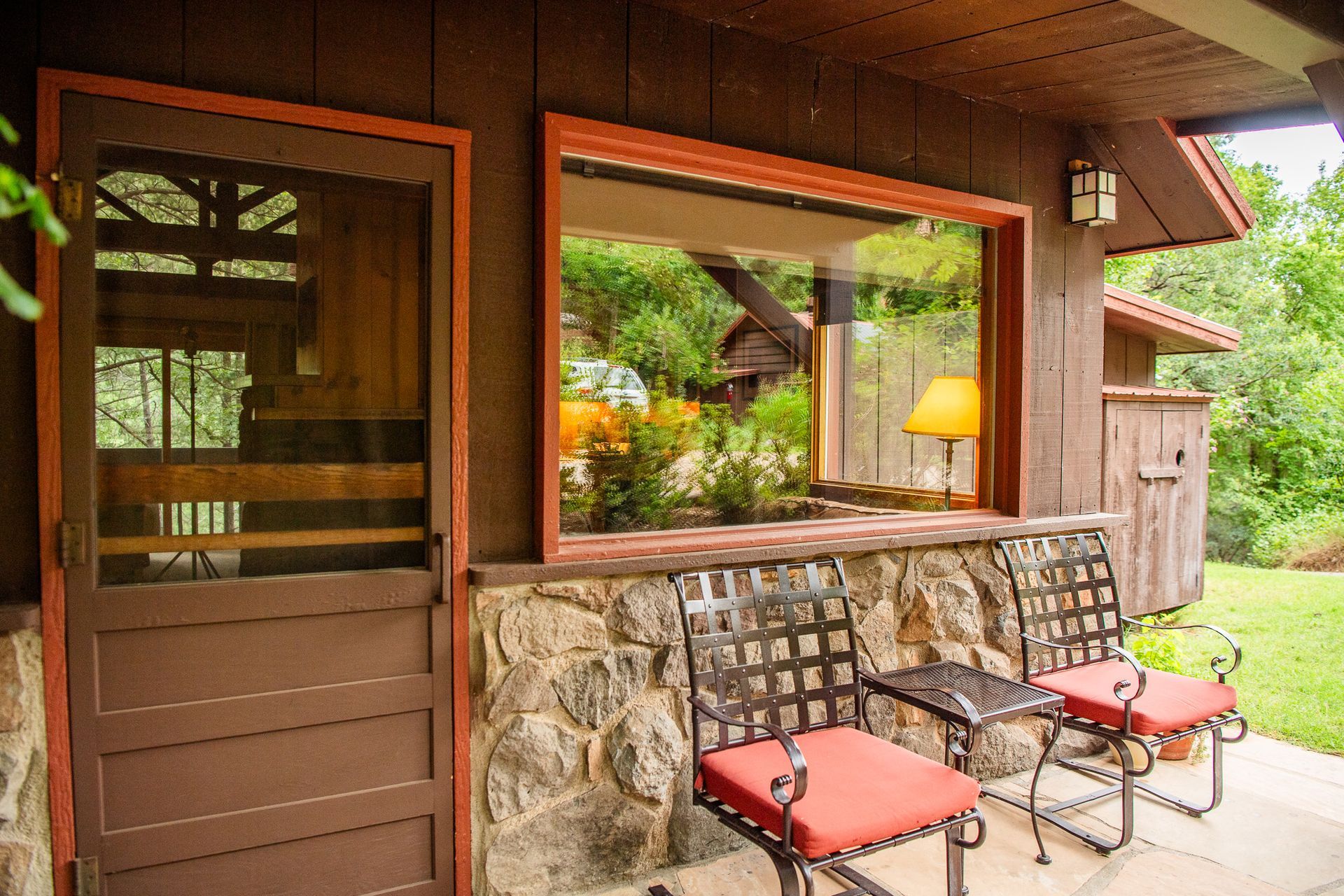 Rustic porch with stone wall, wooden door, and two red-cushioned chairs by a window