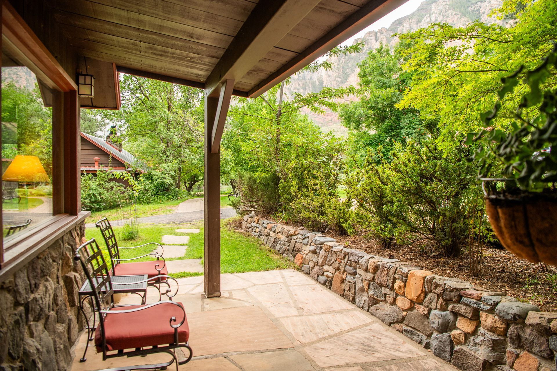 Covered patio with red chairs, stone wall, and lush garden pathway leading into greenery