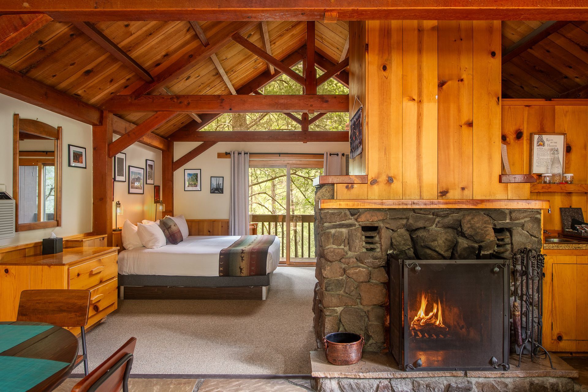Cozy cabin bedroom with a stone fireplace, wood beams, and a bed near a large window.
