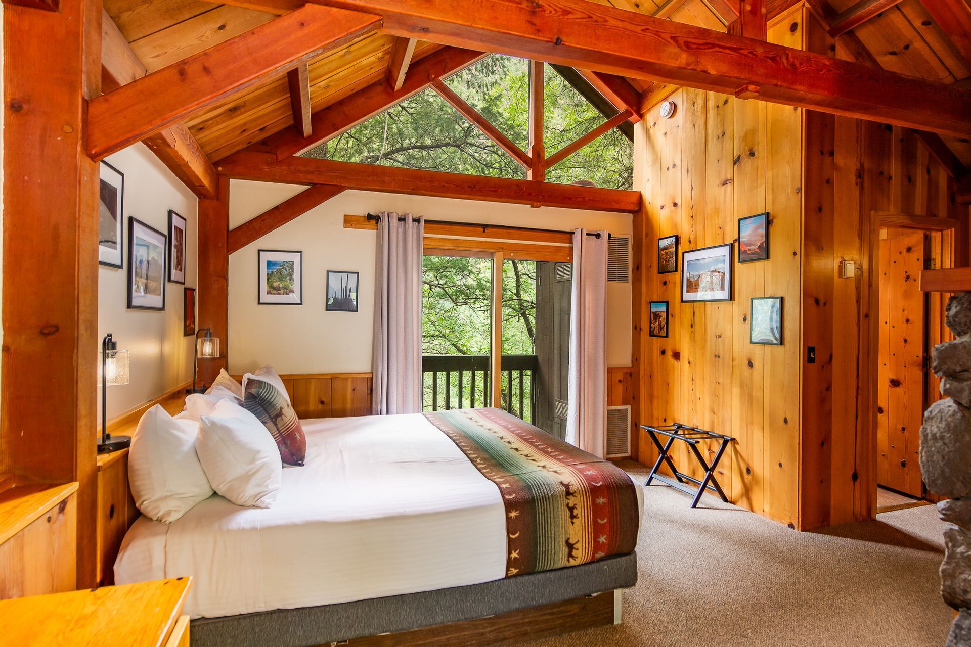 Rustic wooden bedroom with a bed, exposed beams, and balcony doors overlooking greenery