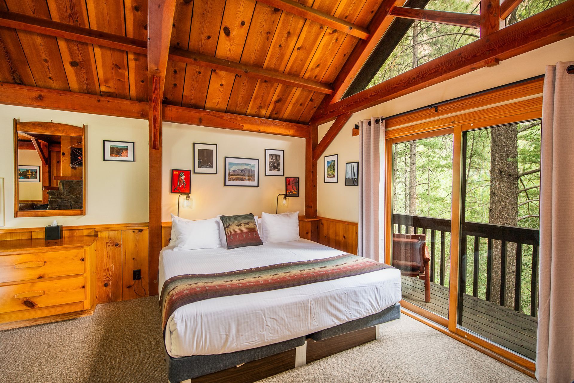 Cozy cabin bedroom with wooden ceiling, white bed, and sliding glass doors to a forest view