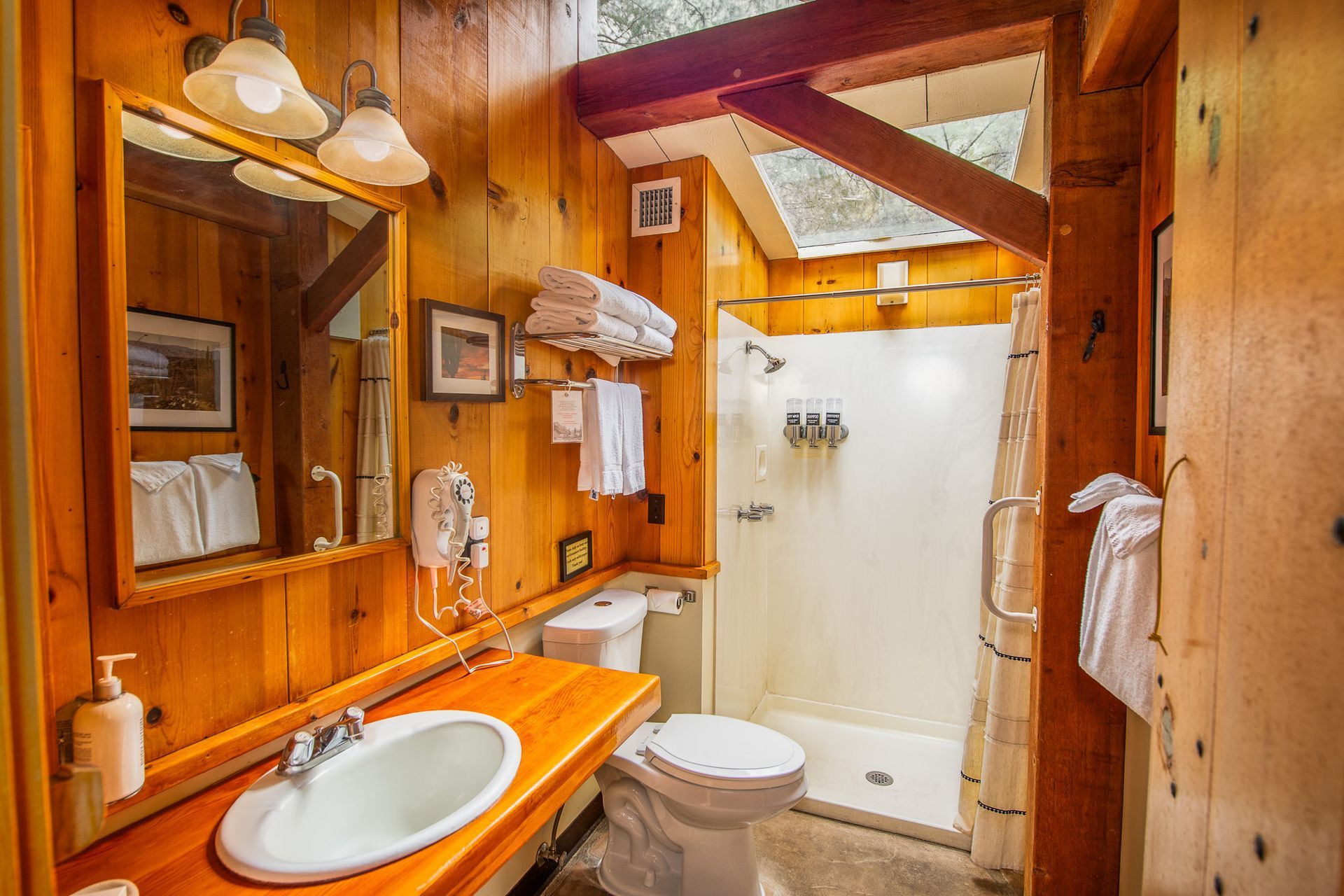 Wood-paneled bathroom with orange vanity, mirror, sink, toilet, and shower stall