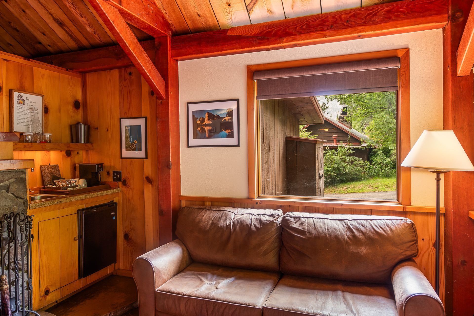 Cozy wood-paneled living room with leather sofa, fireplace nook, and bright window view