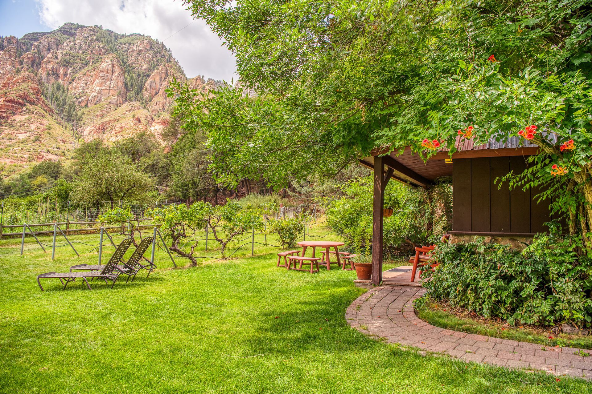 Lush garden with green lawn, picnic table, gazebo, and rocky mountain in the background