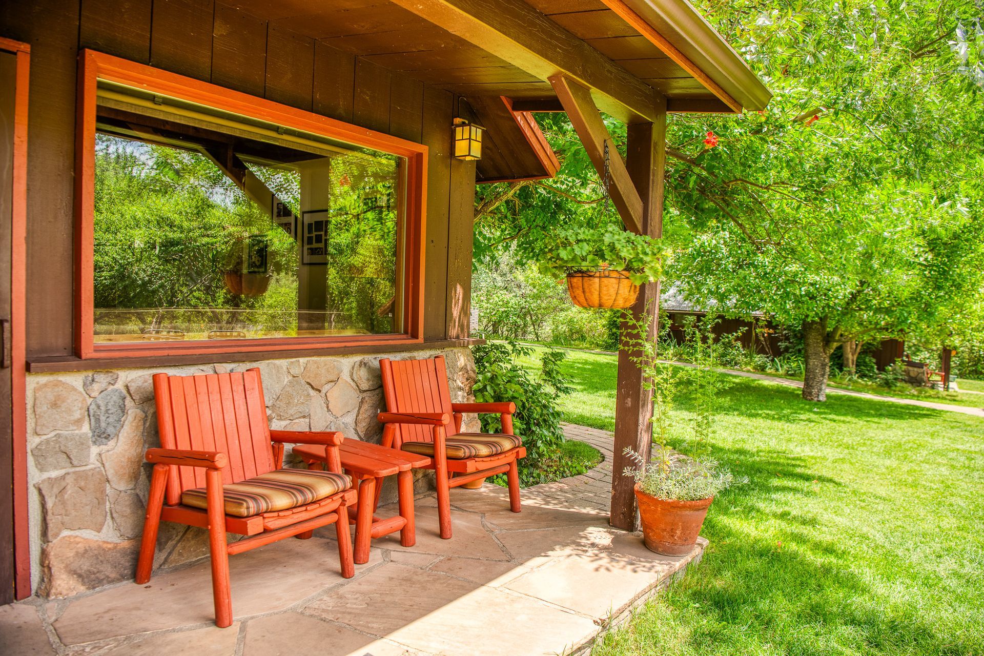 Covered porch with red chairs beside a stone wall, overlooking a green garden and trees.