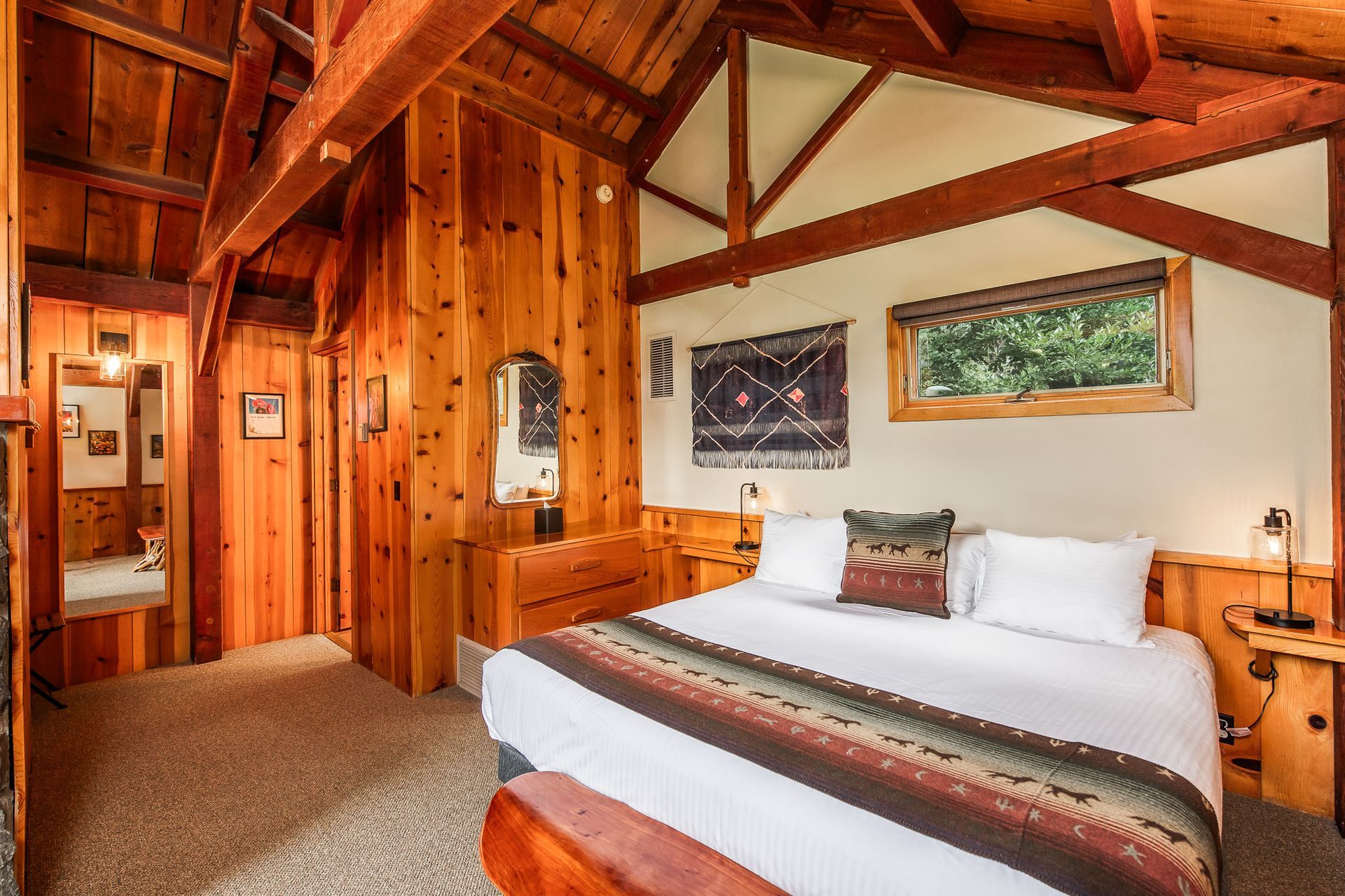 Rustic cabin bedroom with wood-paneled walls, exposed beams, and a white bed by a window