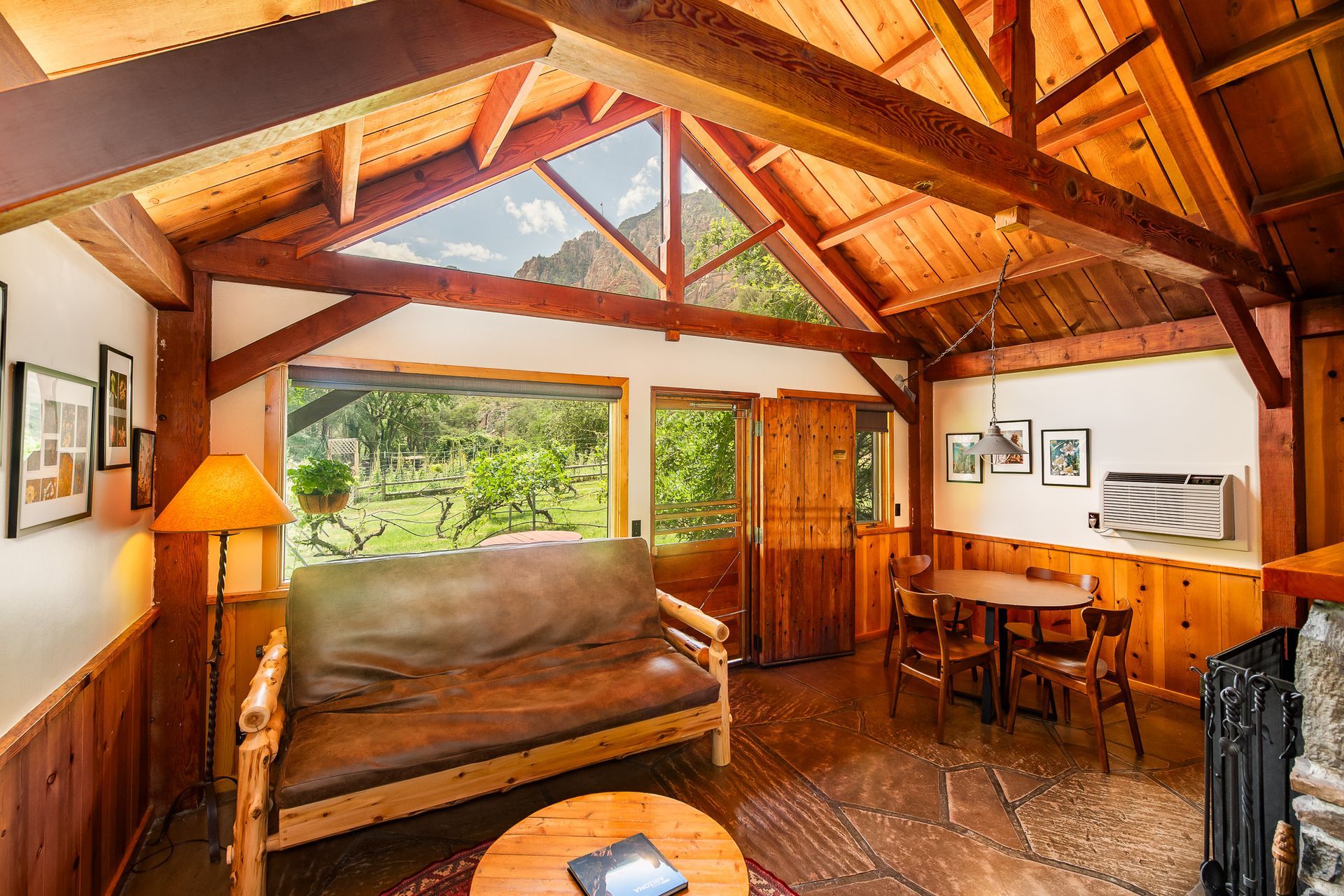 Rustic cabin living room with wooden beams, couch, desk, and skylight window