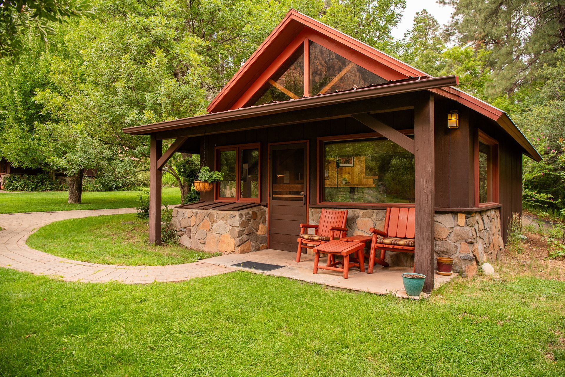 Rustic park pavilion with stone walls, wooden porch, and orange chairs beside a grassy path