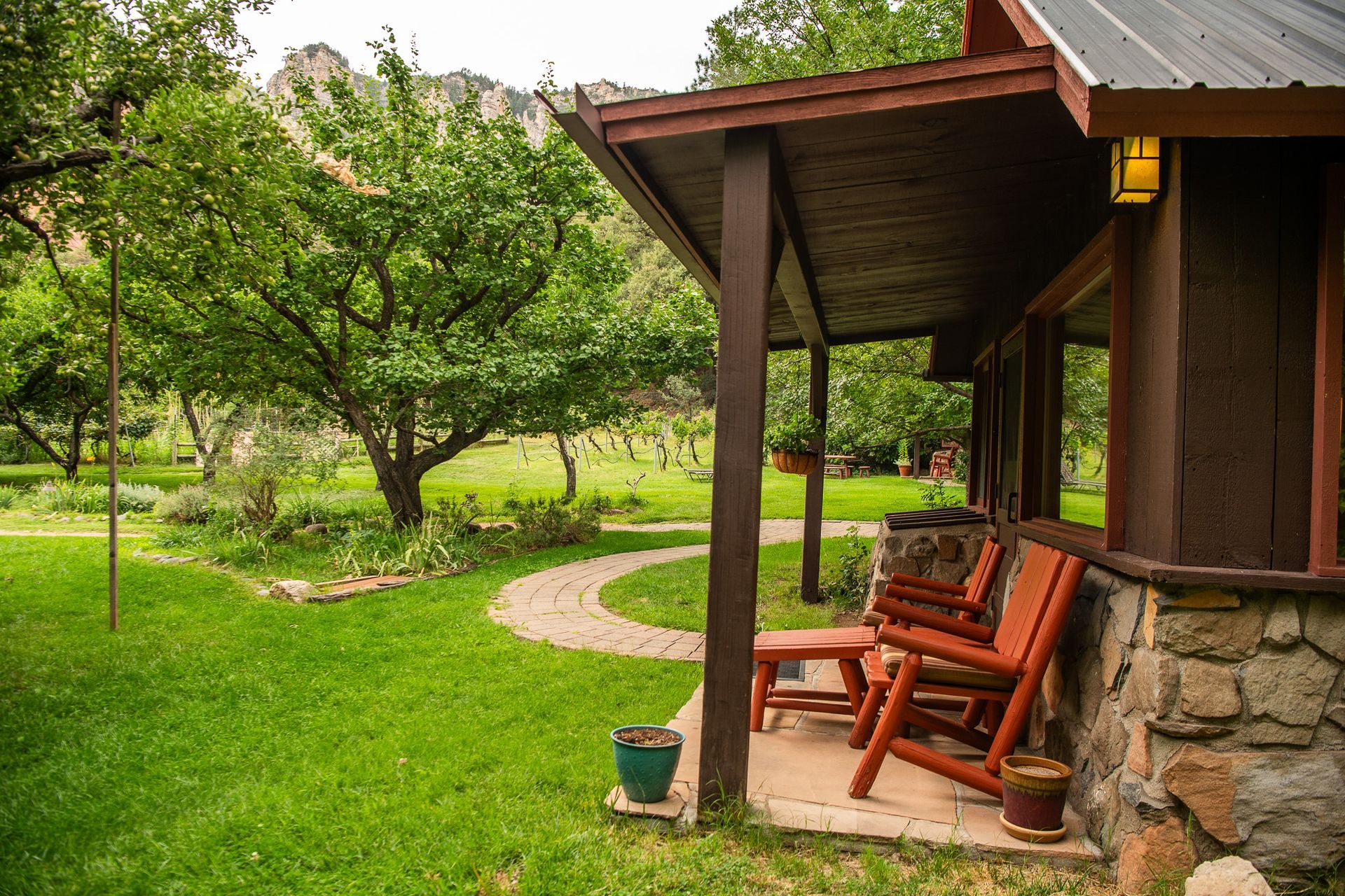 Rustic porch with red chairs beside a lush green orchard and winding garden path