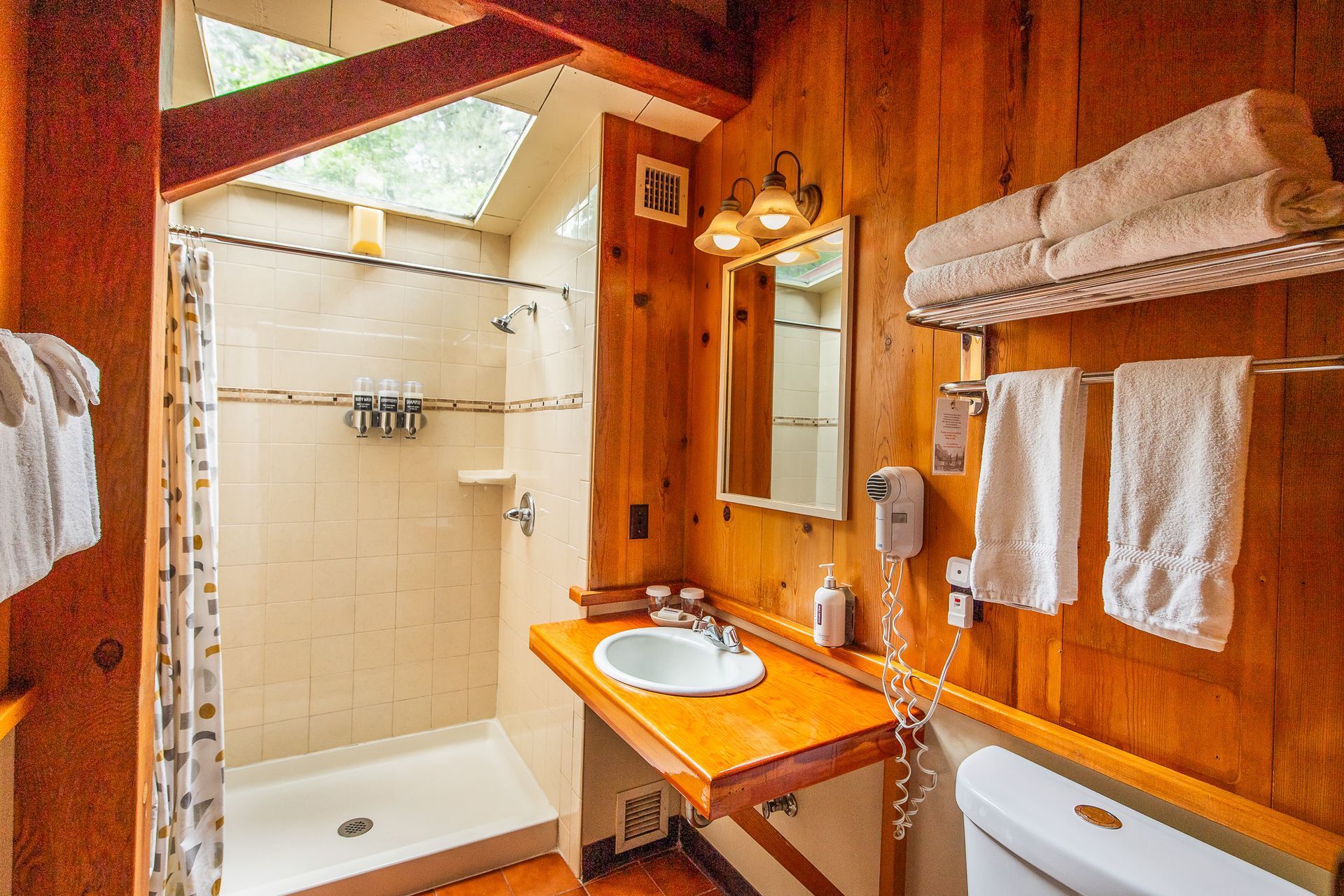 Wood-paneled bathroom with shower stall, sink vanity, mirror, and white towels