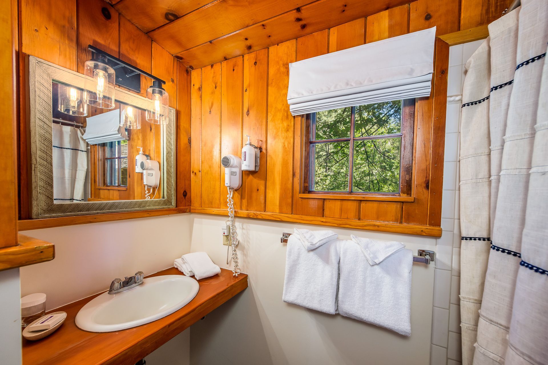 Wood-paneled bathroom with sink, mirror, window, and striped shower curtain
