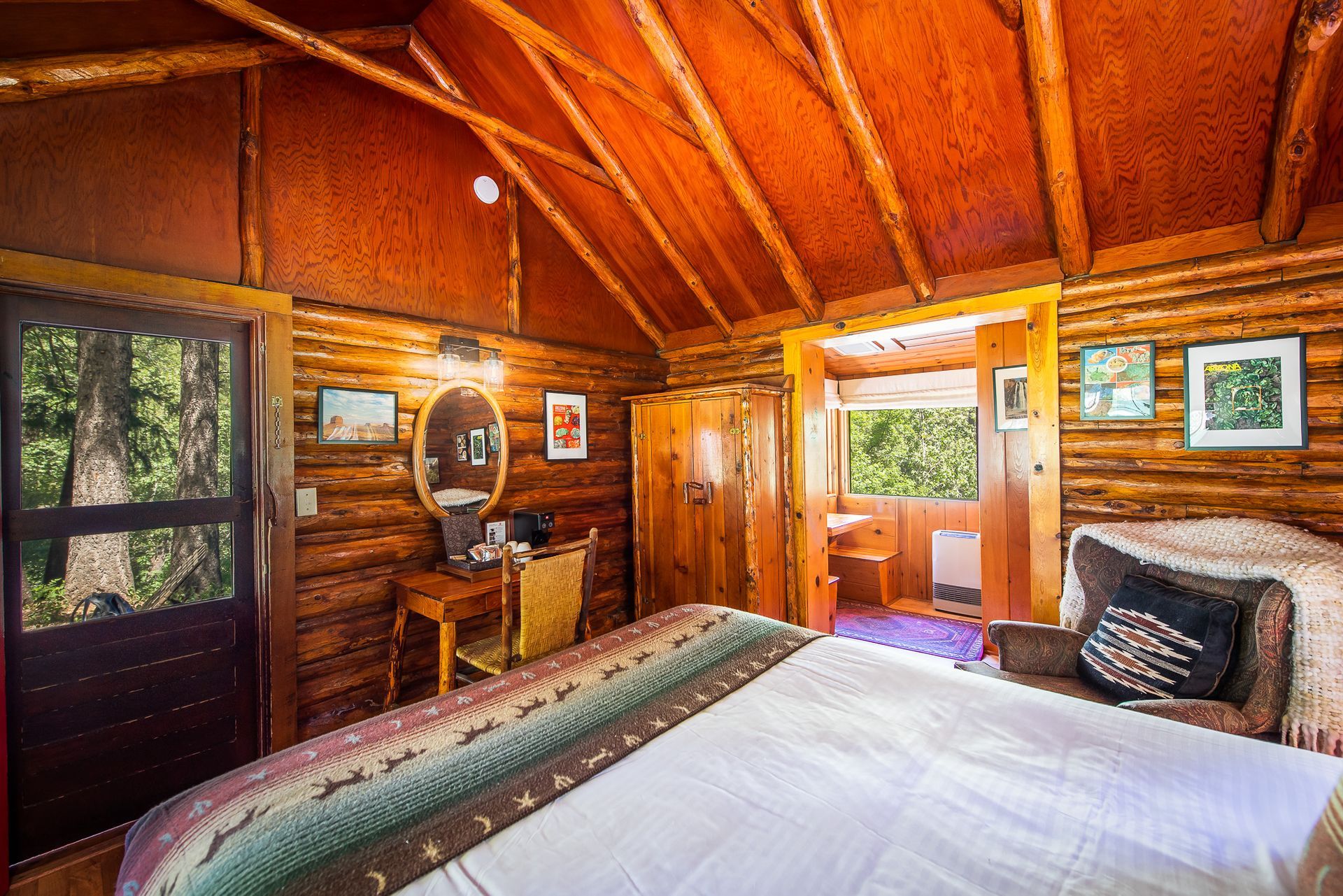 Cozy log cabin bedroom with wood-paneled walls, large bed, desk, and sunlit windows.